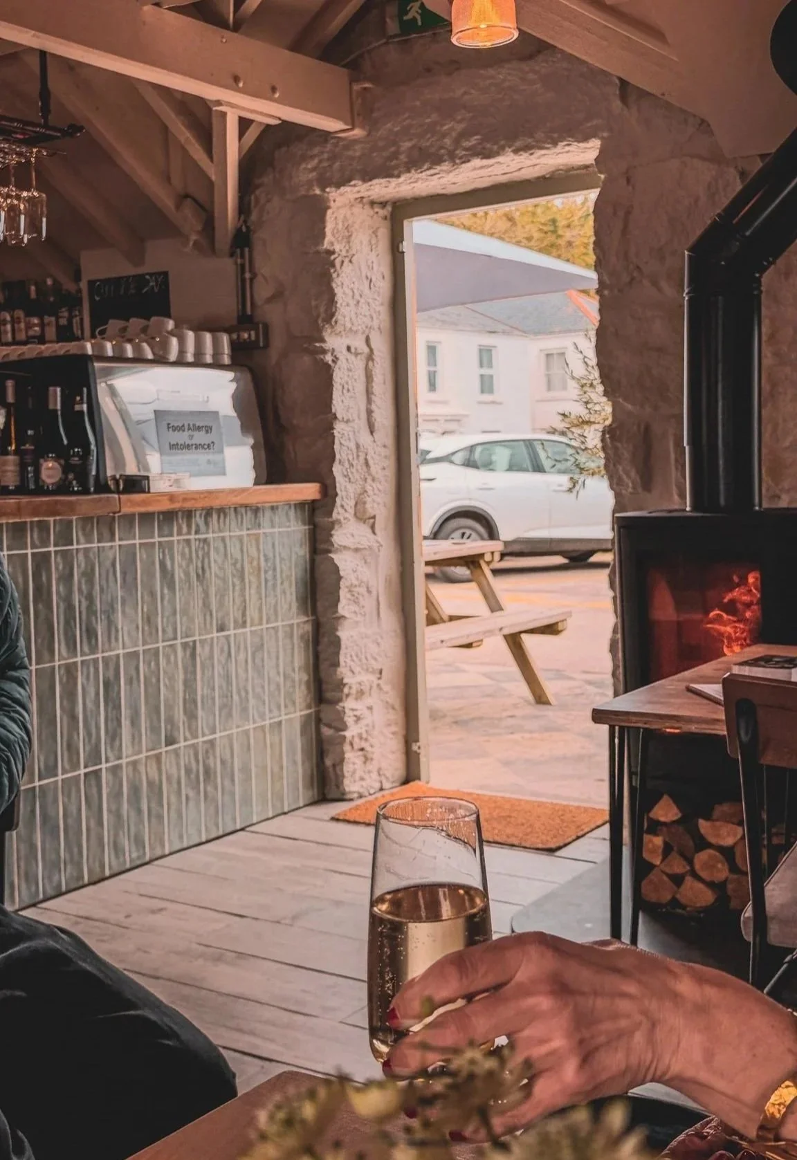 A glass of champagne resting on a wooden table, next to a woodburner