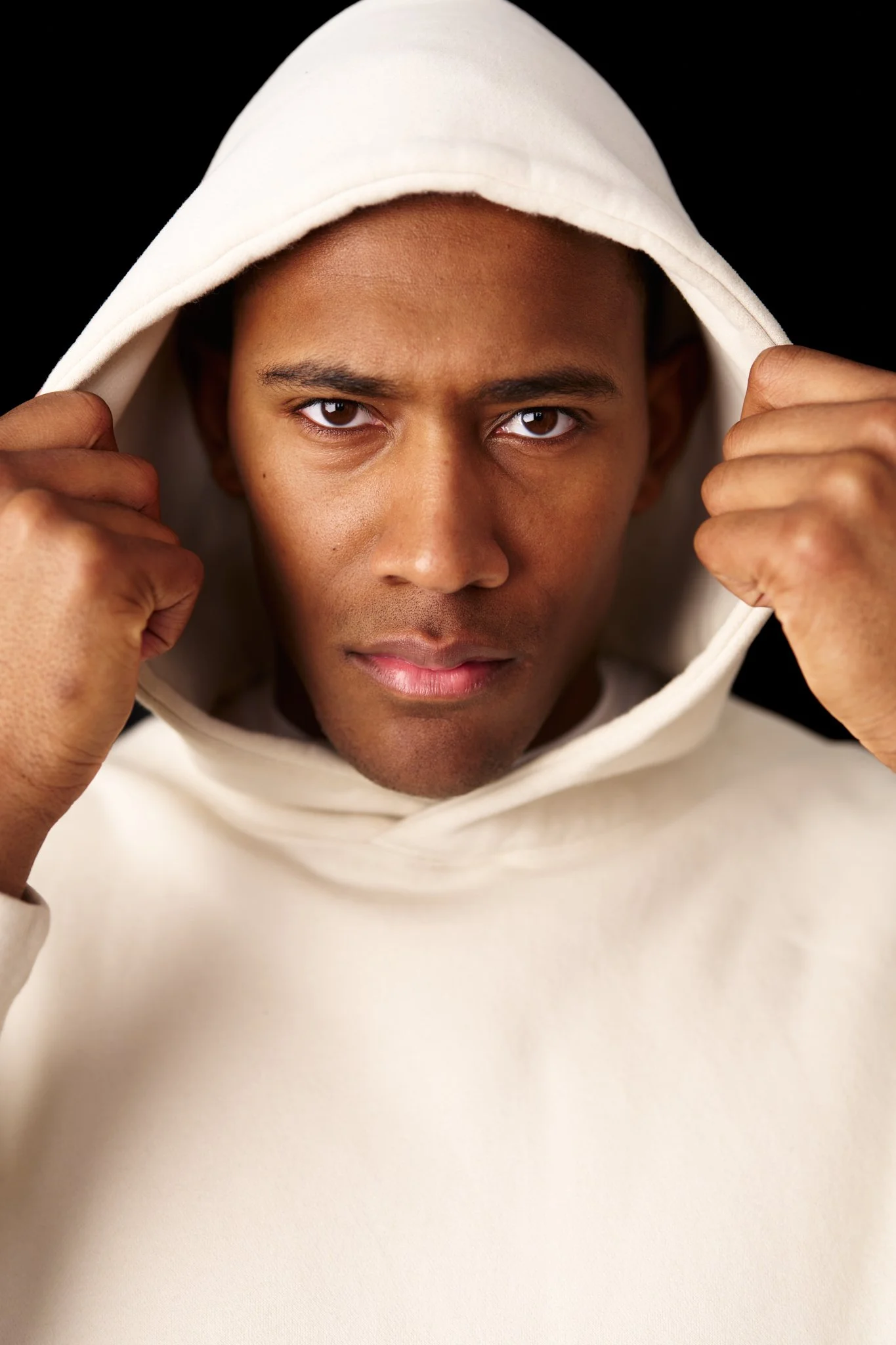 Man wearing a white hoodie looking directly at the camera with a serious expression