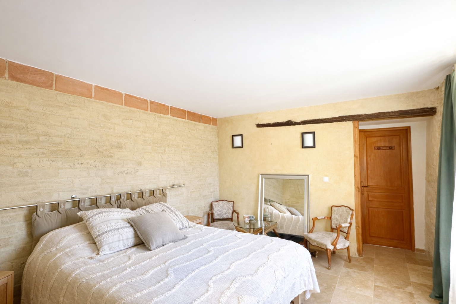 Chambre avec lit, miroir, fauteuils, porte en bois et déco rustique.
