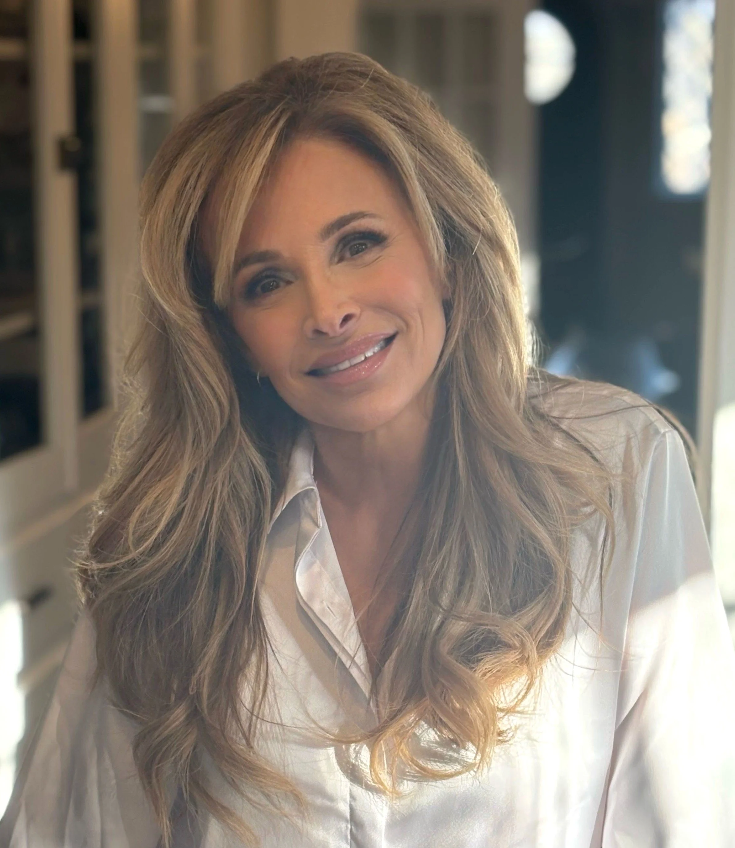 A woman with long, wavy hair smiling at the camera in a well-lit indoor setting.