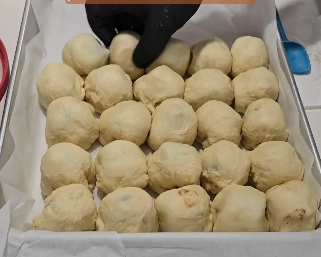 Black gloved hand setting down a roll in the a box of rolled dough for resurrection rolls.