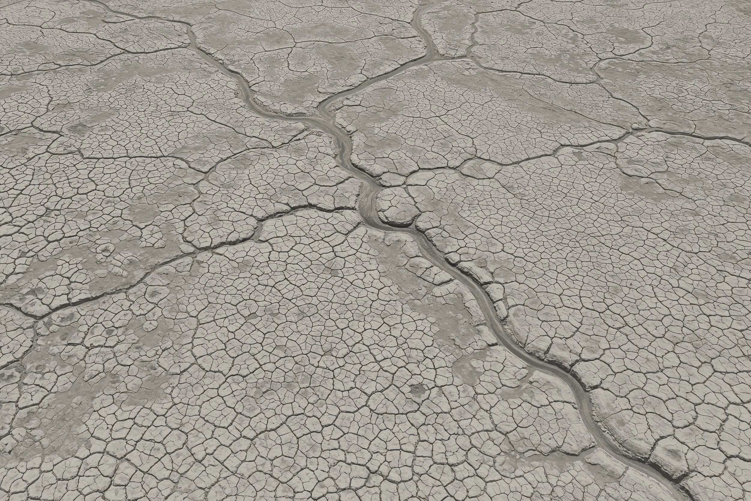 Dry cracked earth with a small, winding stream of water flowing through the center.
