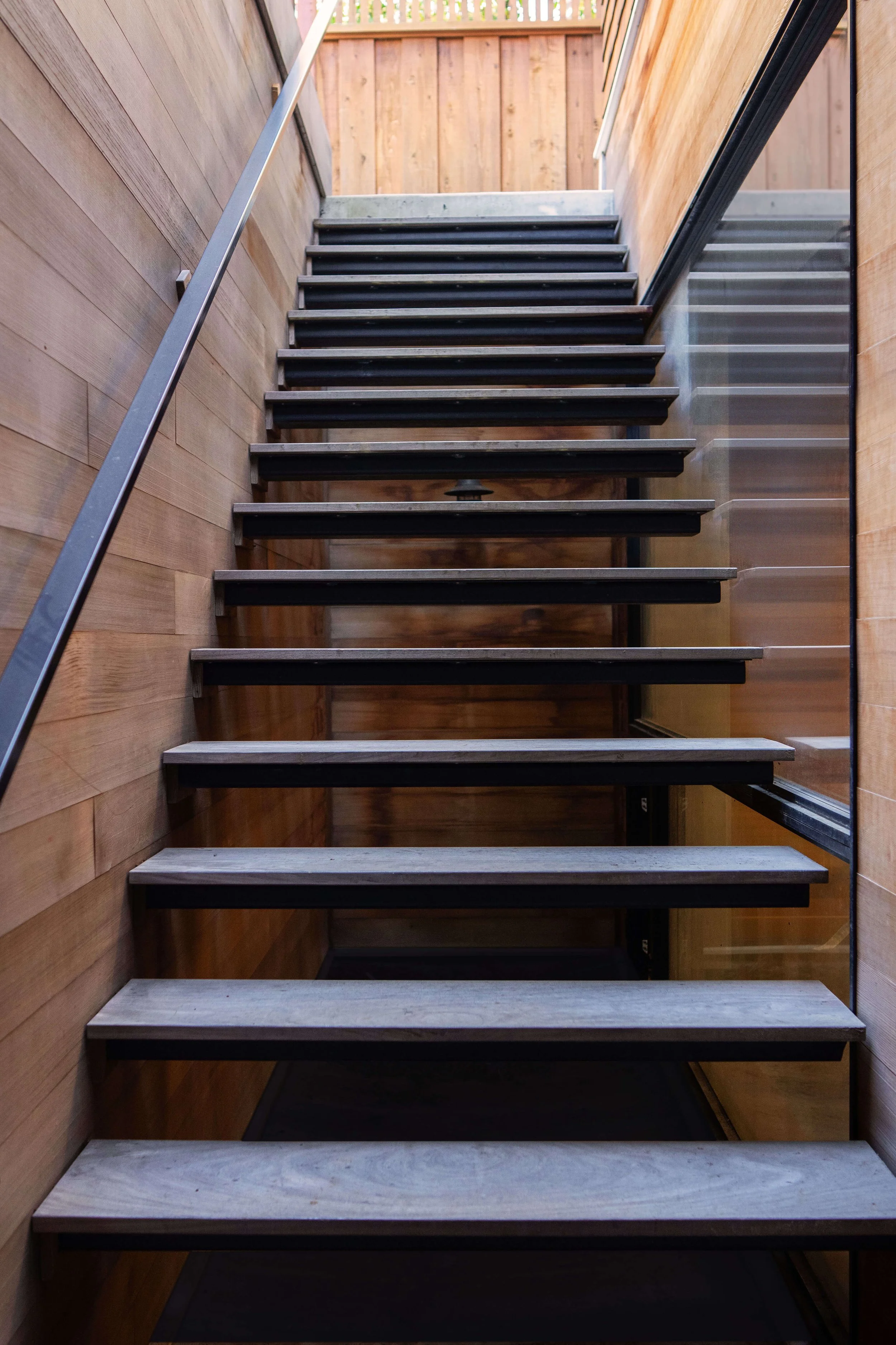 Floating concrete staircase with wooden steps, and black risers going from basement to backyard outdoor kitchen.