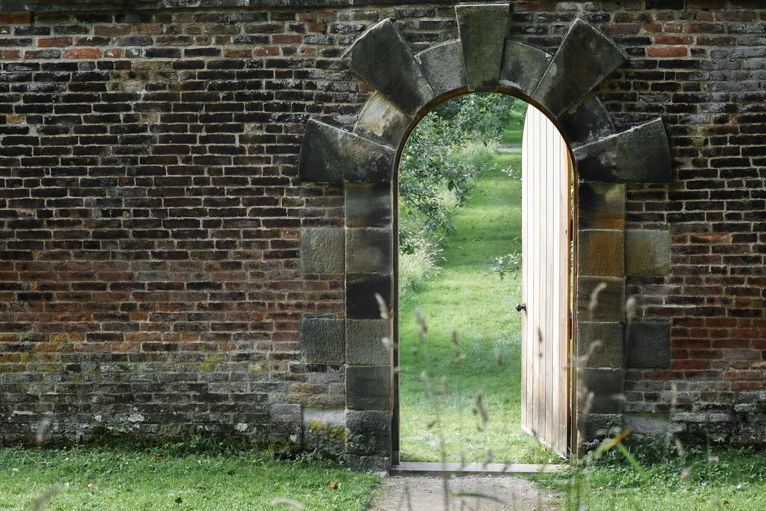 Traditional brick garden wall with arched doorway leading into a garden