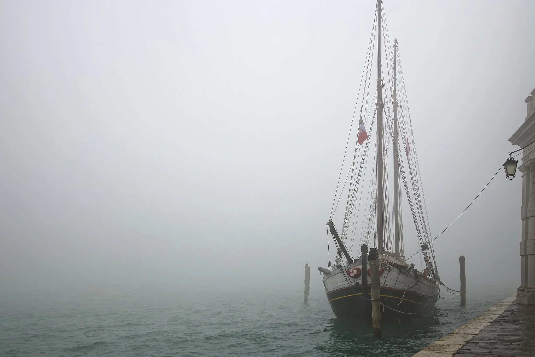A boat docked at a foggy harbor, with the water and a stone walkway visible. Venice Italy.