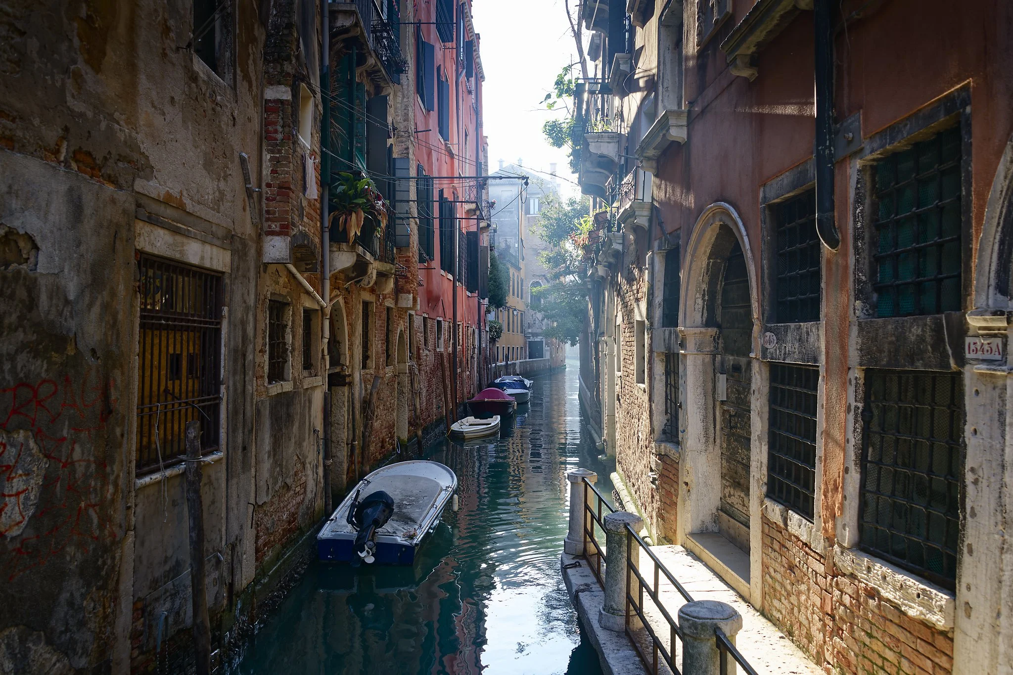 A narrow canal with small boats docked along brick and stucco buildings in Venice, Italy.