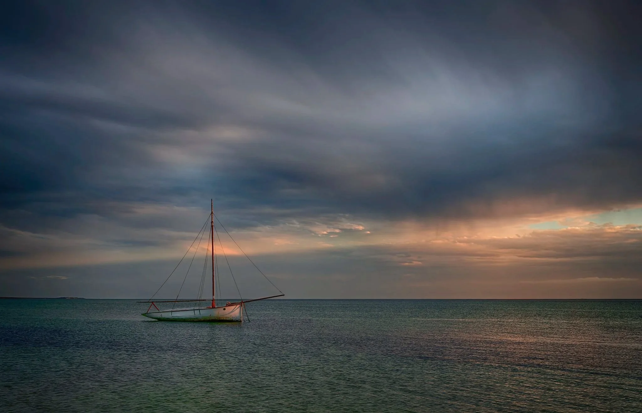 A sailboat capsized in calm ocean waters during sunset, with dramatic clouds in the sky. Exmouth Western Australia.