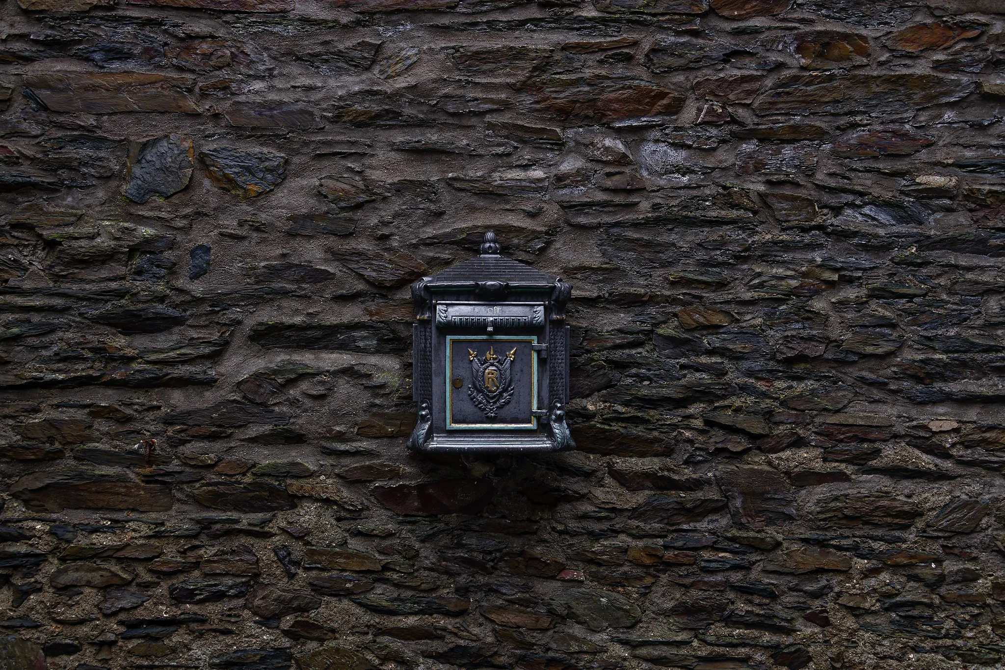 A vintage black mailbox mounted on a dark stone wall. Germany.