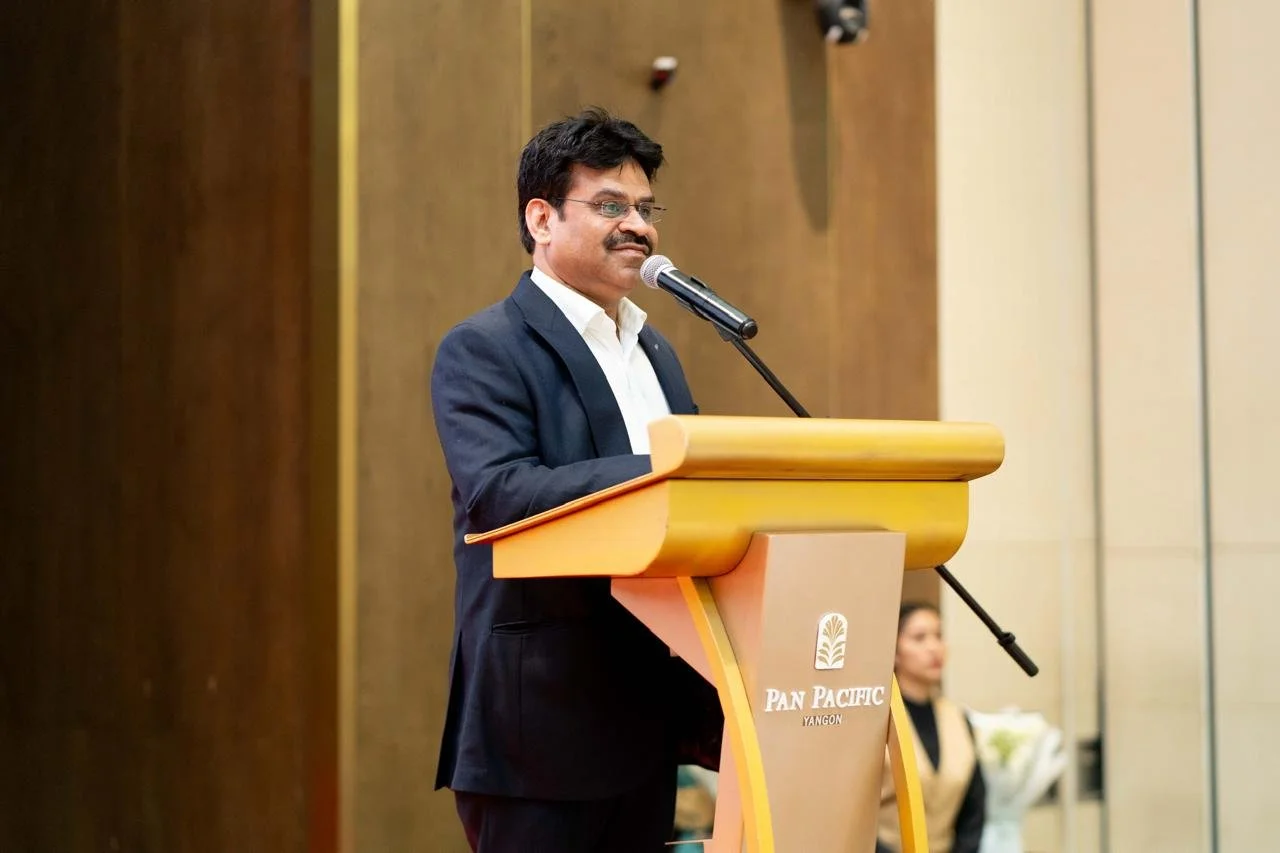 A man in a suit speaking at a podium with a microphone at the Pan Pacific hotel in Yangon.