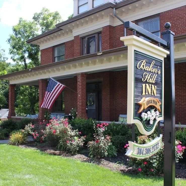 Exterior view of Baker's Hill Inn with a garden, American flag, and a sign displaying the inn's name and contact number.