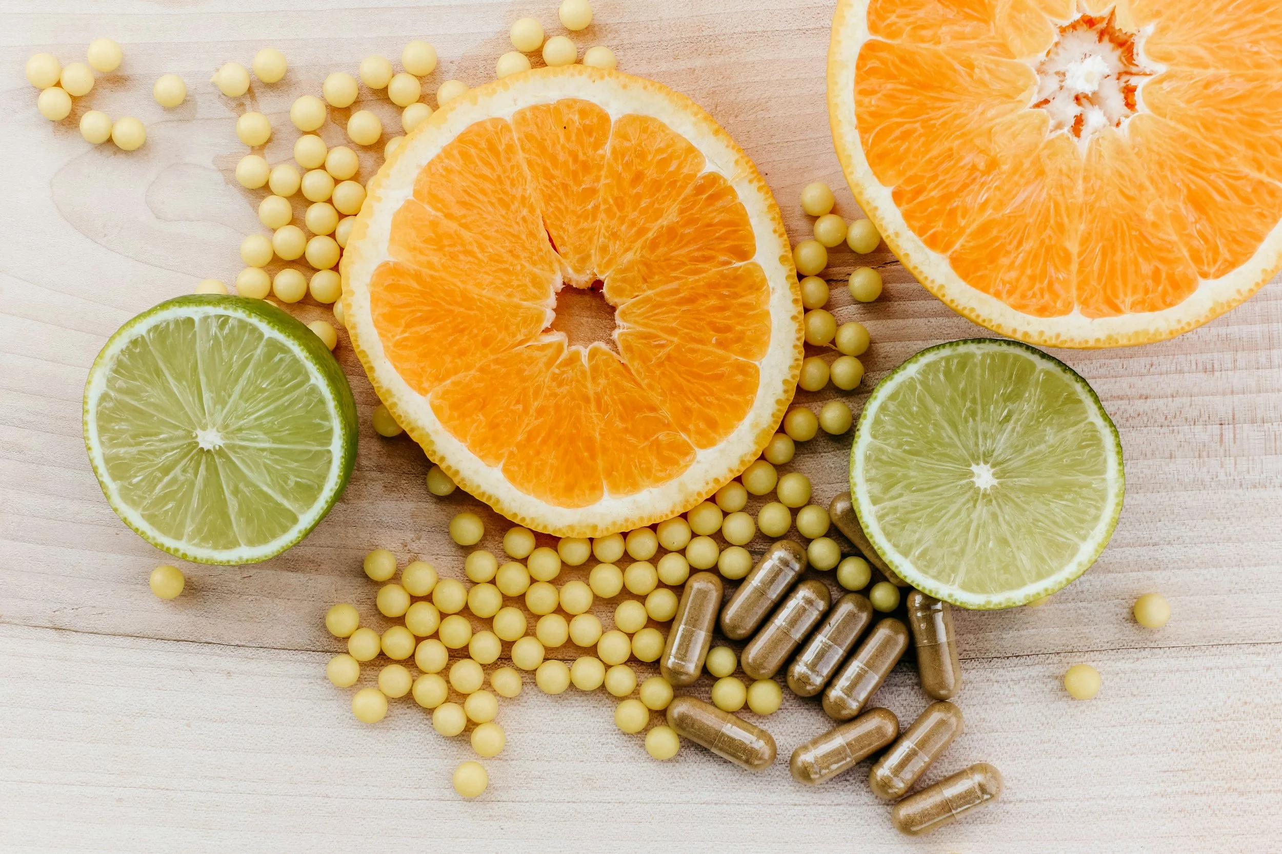 Slices of orange and lime with yellow pills and supplements scattered on a wooden surface.