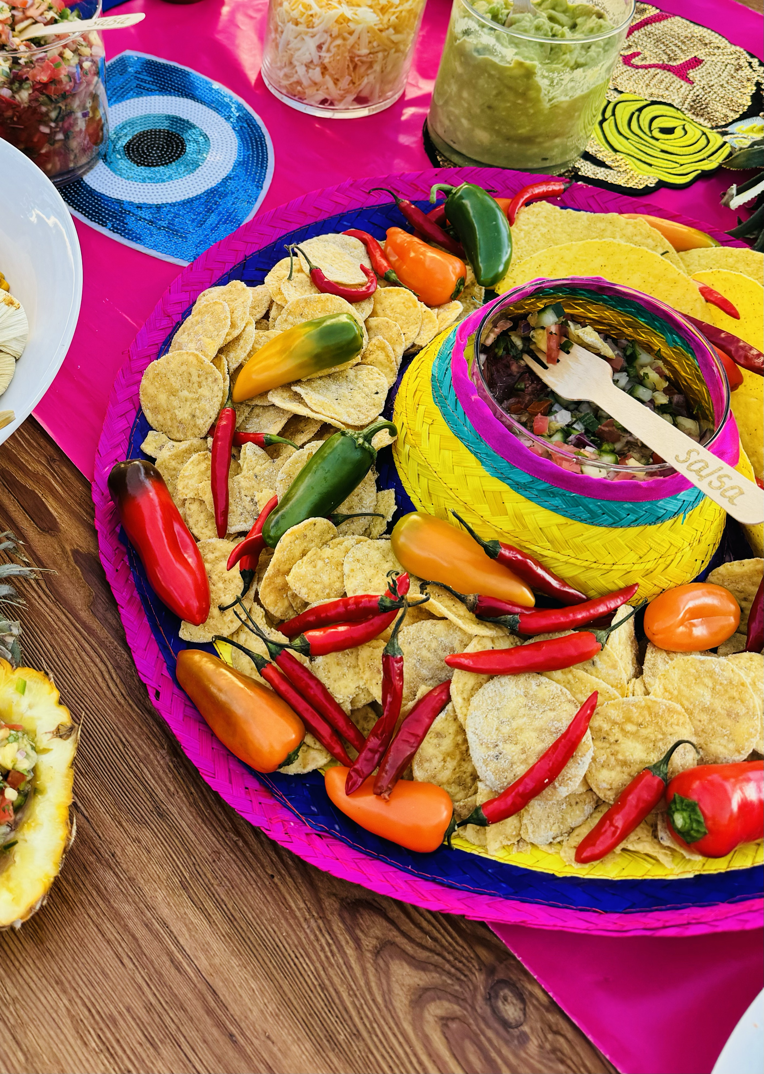 Colorful Mexican food spread with tri-colored chips, jalapeños, and salsa on a pink tablecloth.