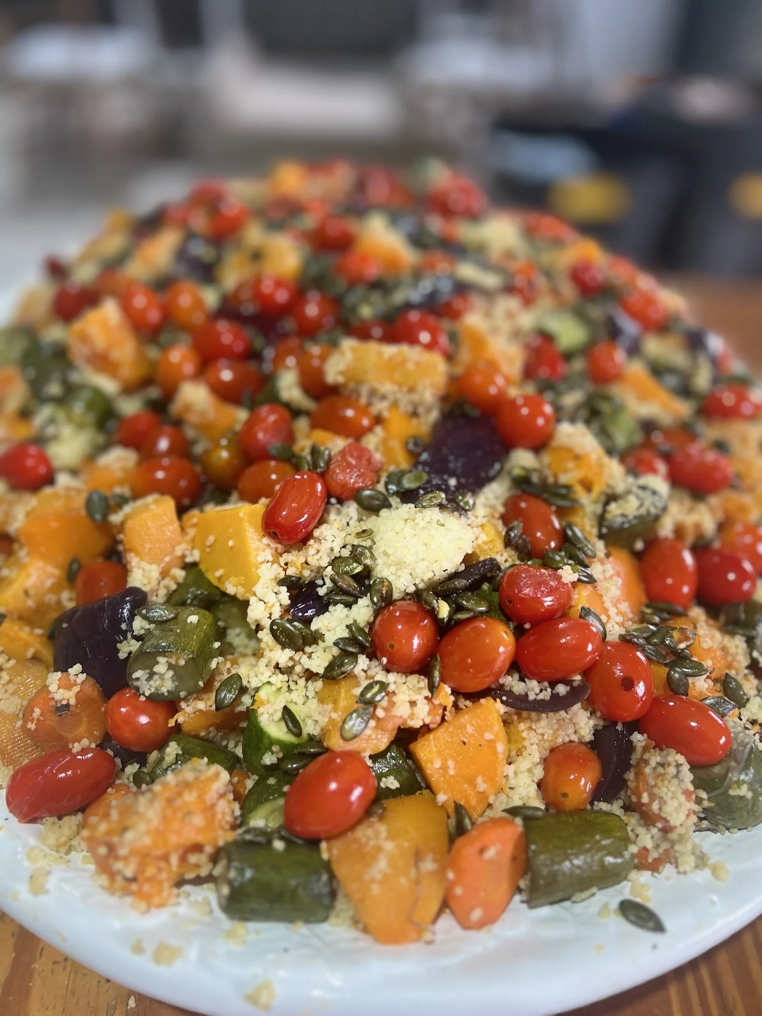 Close-up of a colorful vegetable and grain salad with cherry tomatoes, squash, zucchini, seeds, and cheese on a white plate.