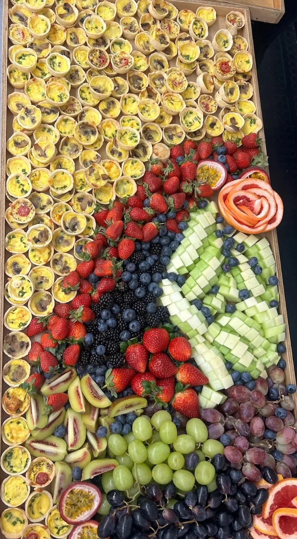 Tray of assorted fresh fruits and mini quiches with various toppings.