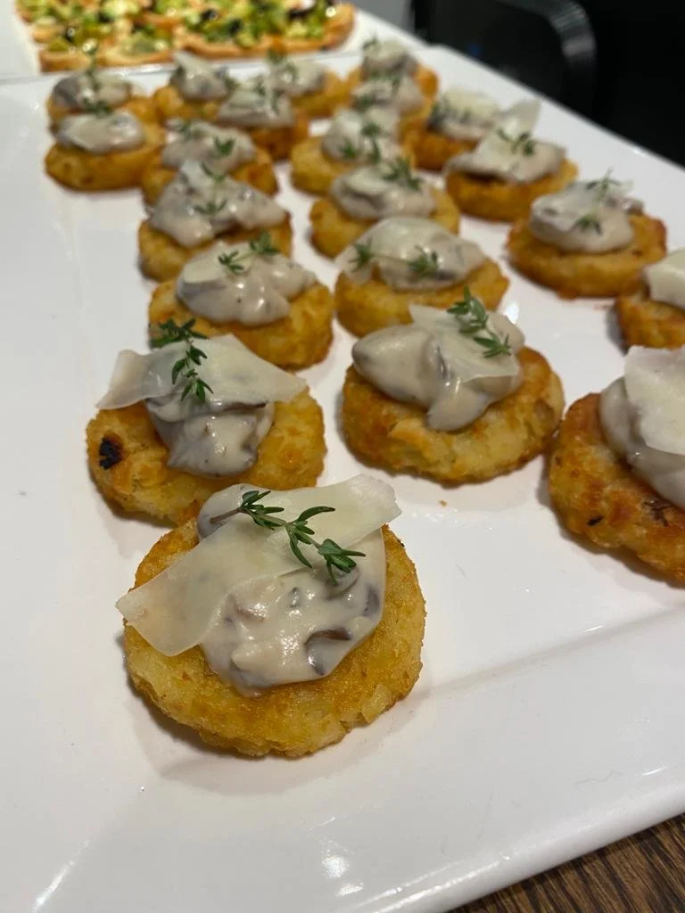 Close-up of bite-sized appetizers on a white serving tray, topped with creamy mushroom sauce, cheese, and garnished with small herbs.