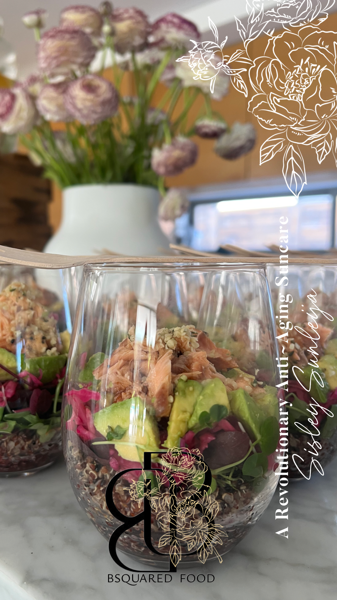 Salad in a glass bowl with avocado, salmon, and mixed greens, placed on a marble surface with a blurred background of flowers in a vase and a window.