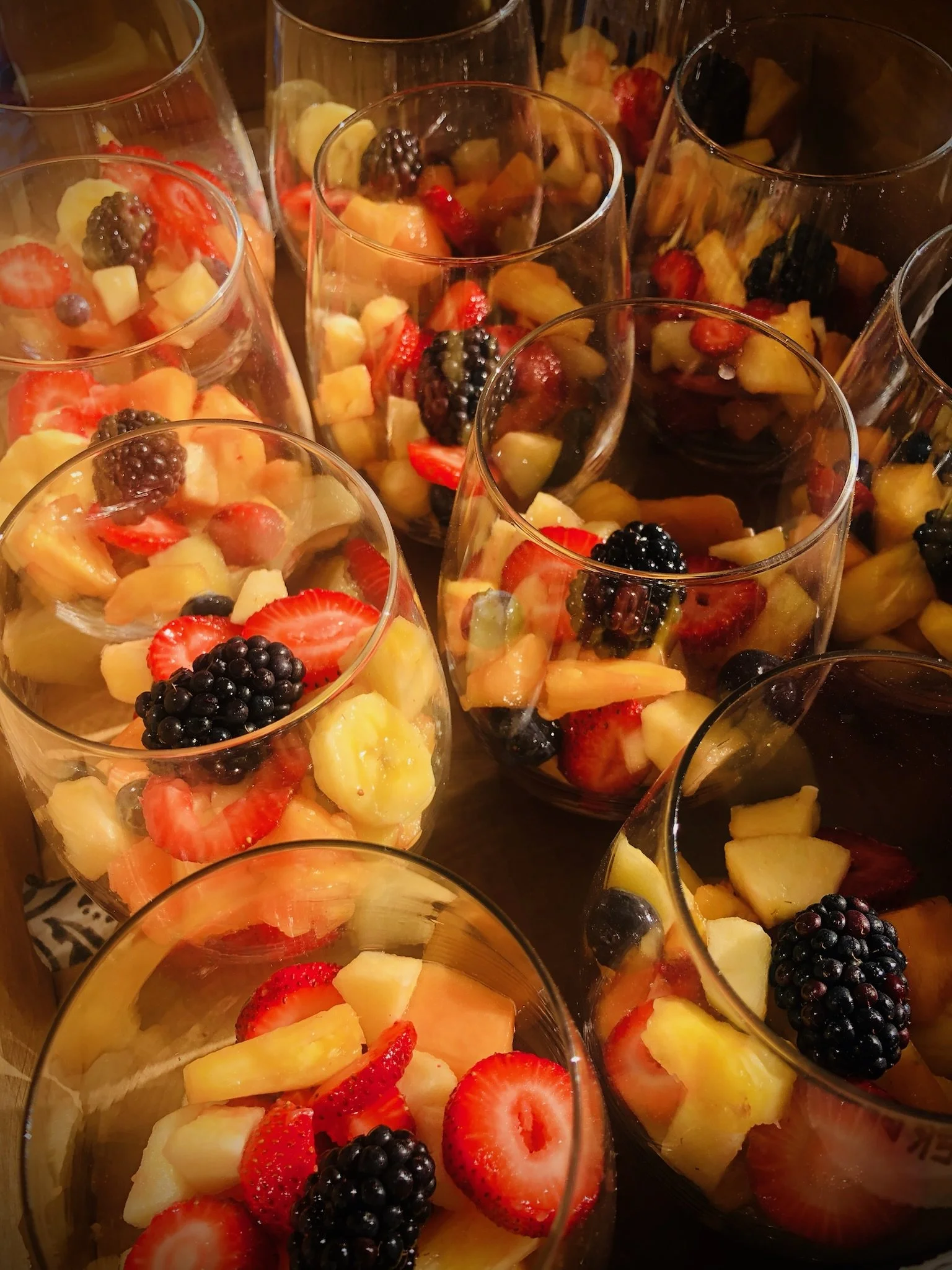 Multiple glasses filled with fresh fruit salad containing strawberries, blackberries, pineapple, and melon.