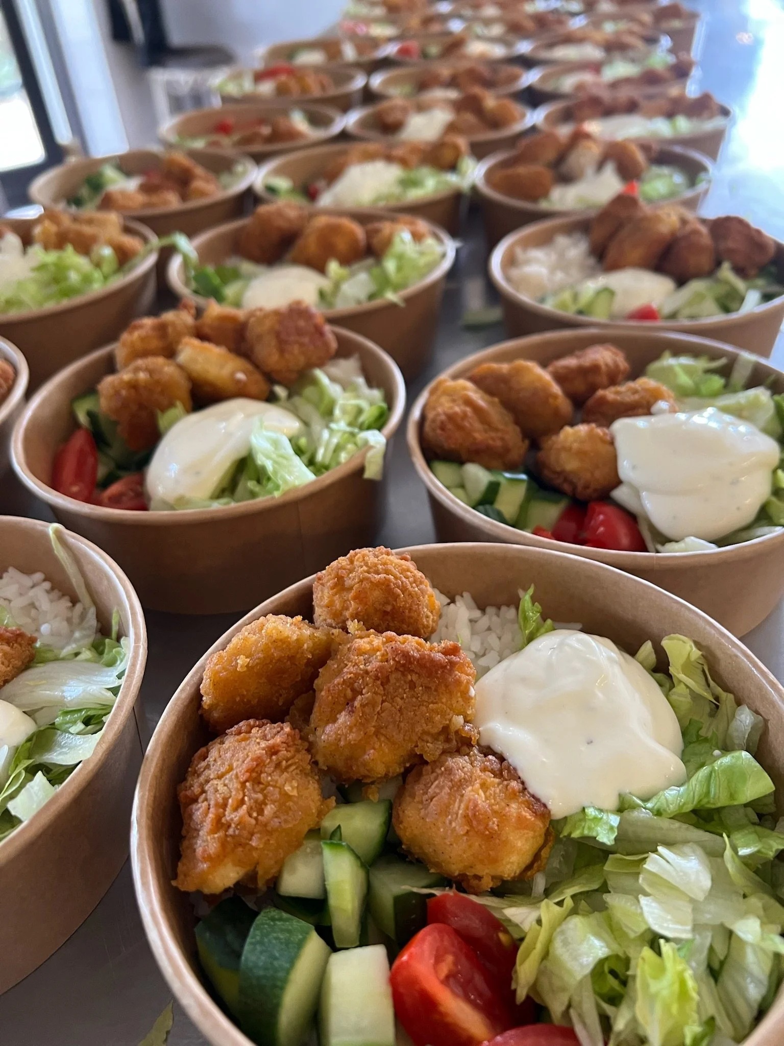 Multiple bowls of salad with fried chicken pieces, cherry tomatoes, cucumbers, lettuce, and a creamy dressing on top.
