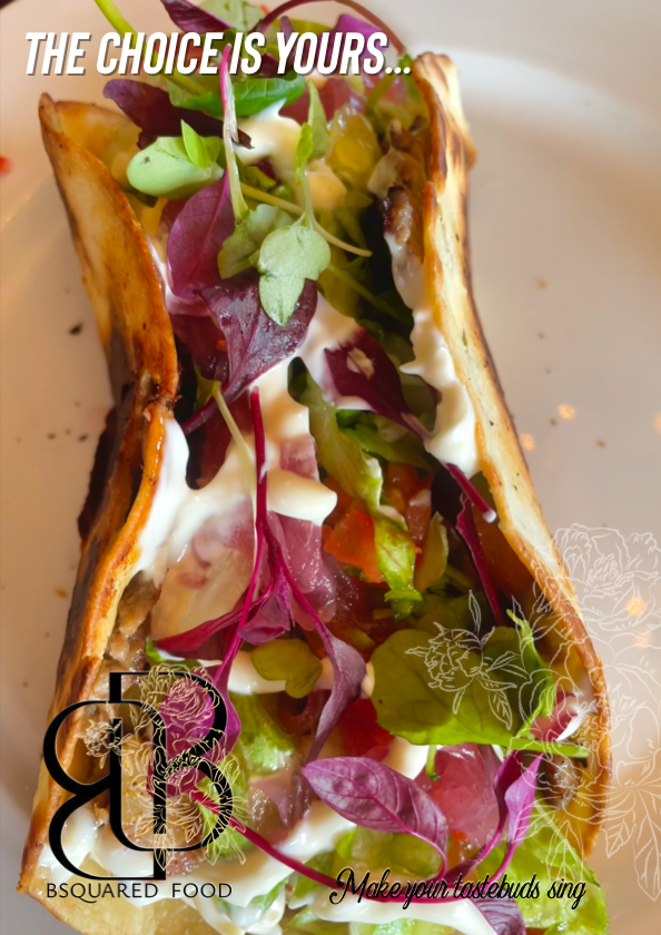 A close-up of a taco filled with colorful greens, diced vegetables, creamy sauce, and a toasted taco shell on a white plate.