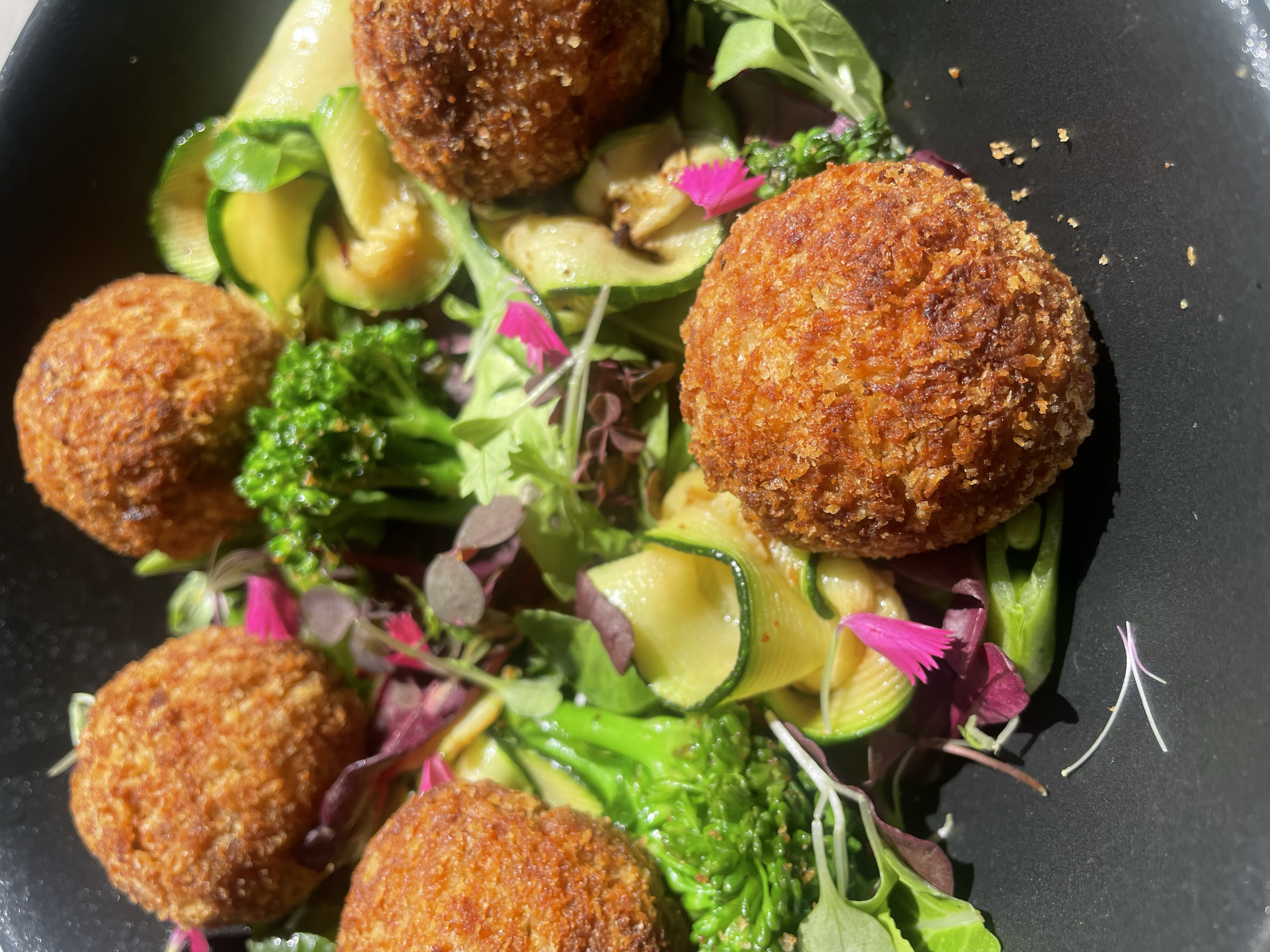 Fried croquettes served with a side of mixed greens and vegetables, garnished with pink edible flowers.