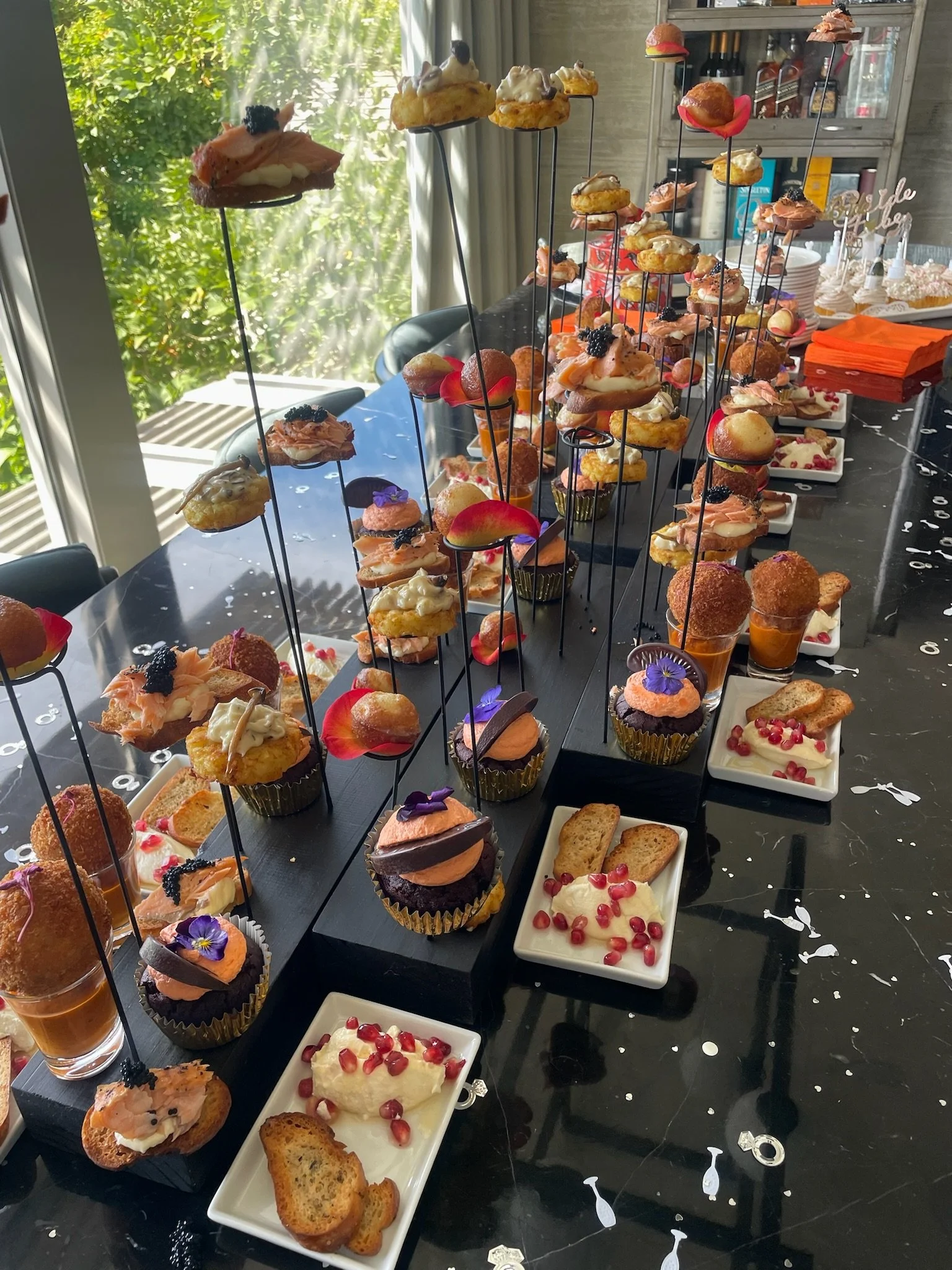 Display of assorted small desserts and appetizers on black wooden boards and white plates at a party table.