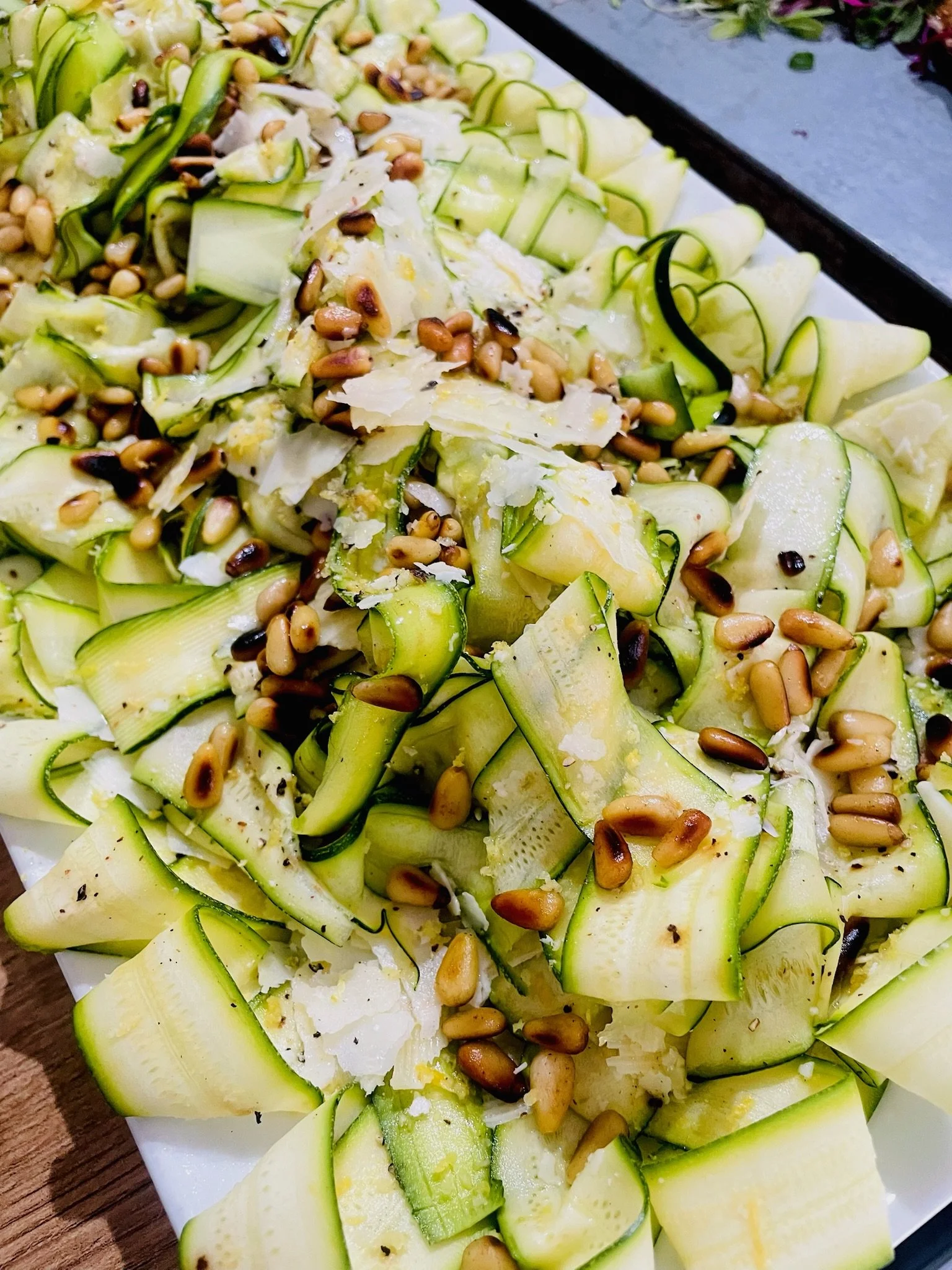 Zucchini noodles topped with pine nuts and cheese on a white platter.