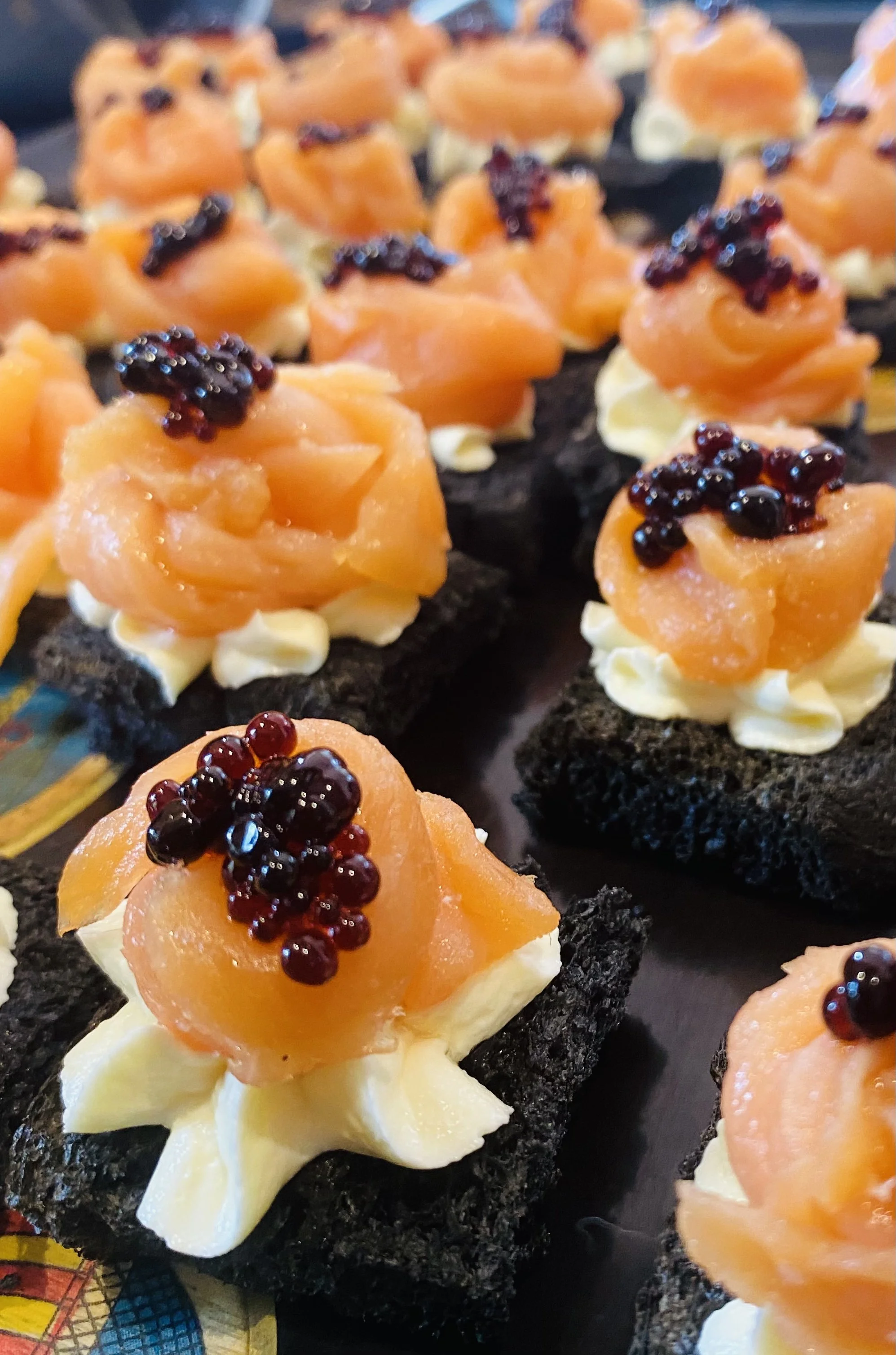 Canapés with black bread bases topped with cream, smoked salmon, and black caviar.
