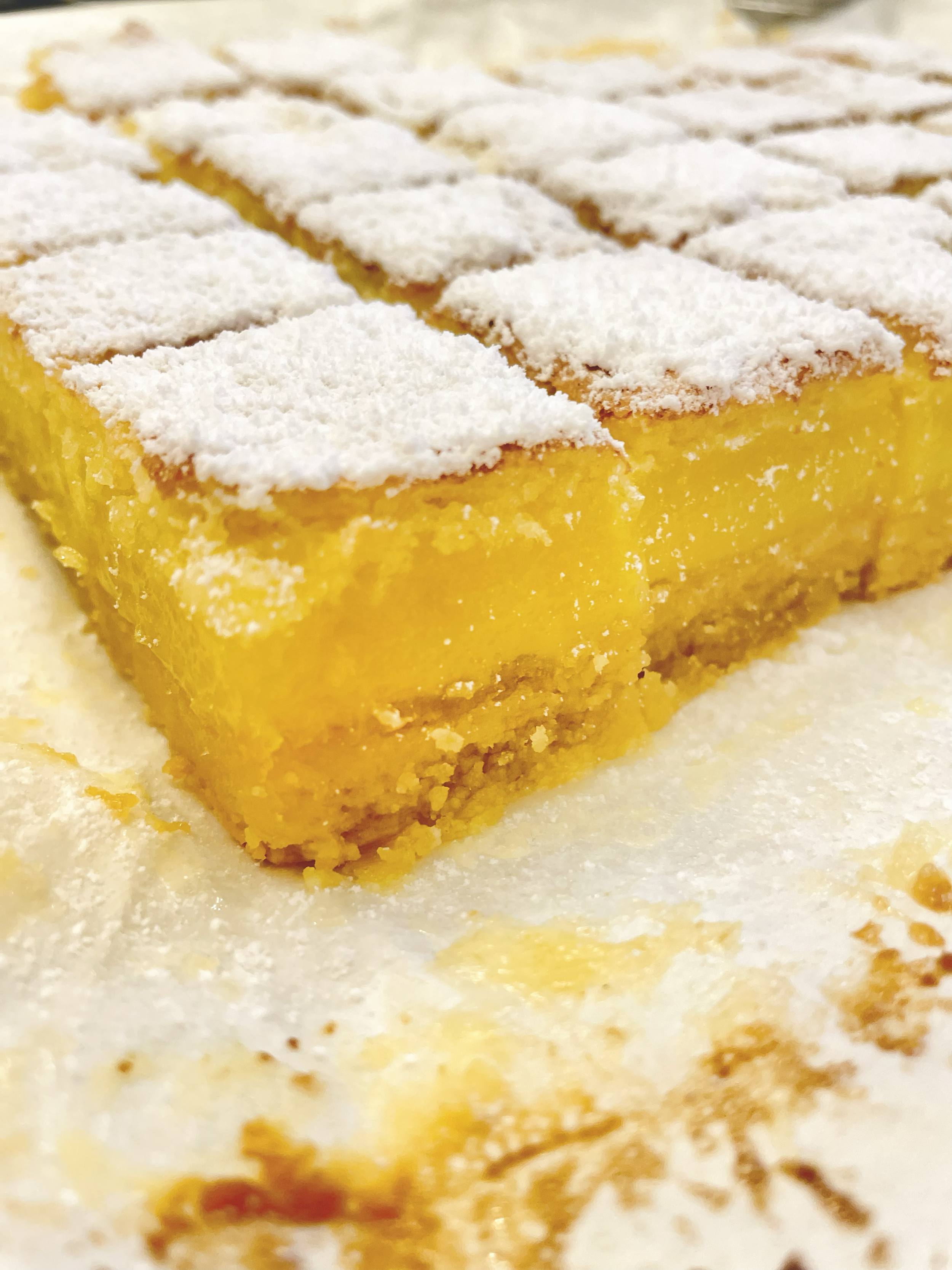 Close-up of a lemon bar with a powdered sugar topping, showing a bright yellow filling and a crumbly base.