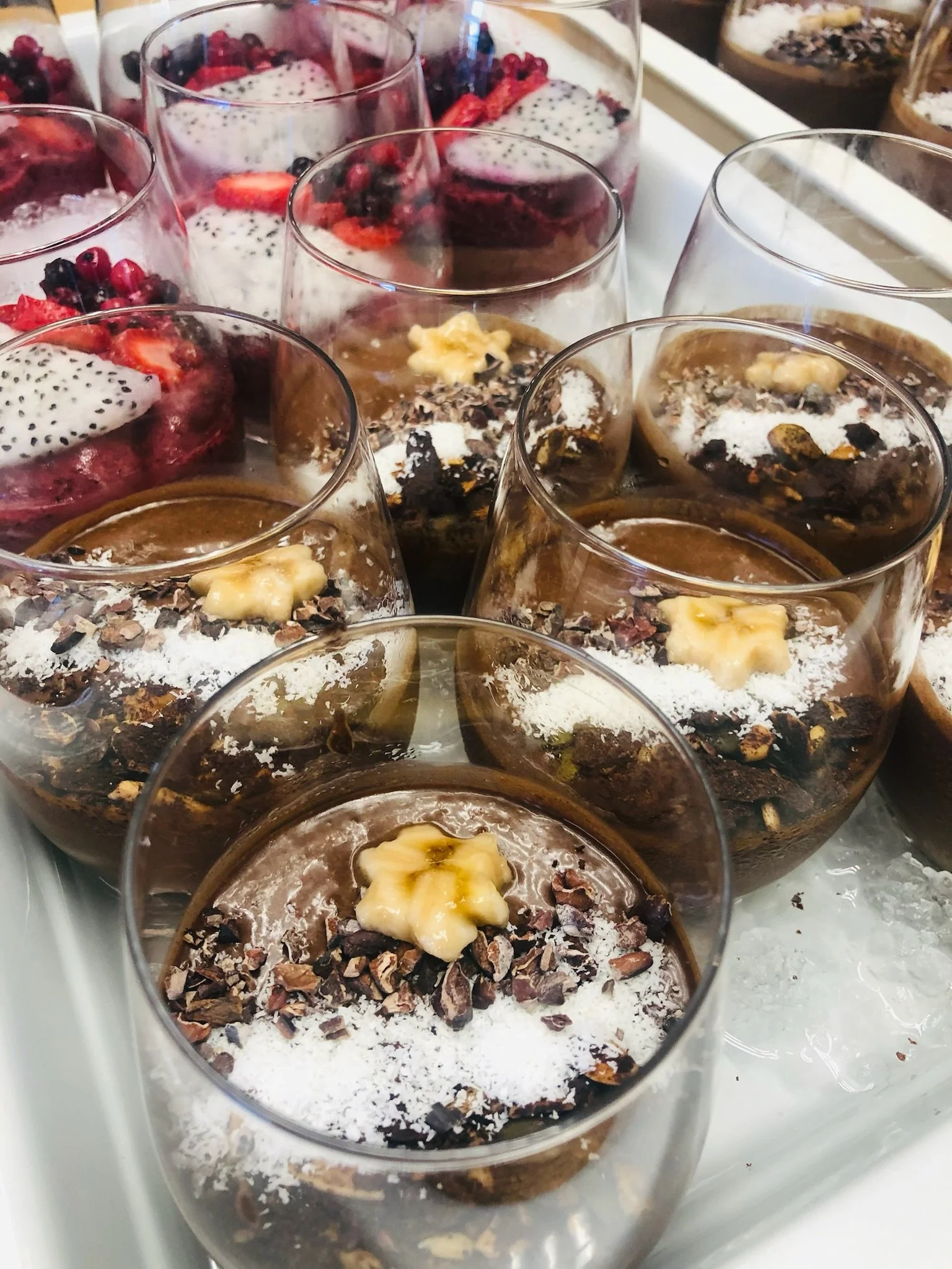 Close-up of chocolate smoothie topped with chopped almonds, grated coconut, and a walnut, served in clear glasses.
