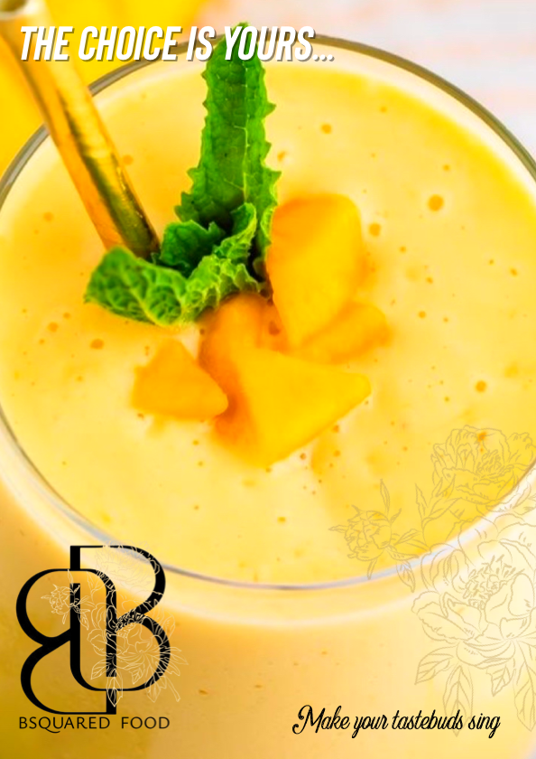A yellow fruit smoothie garnished with a mint leaf and fruit pieces in a glass.