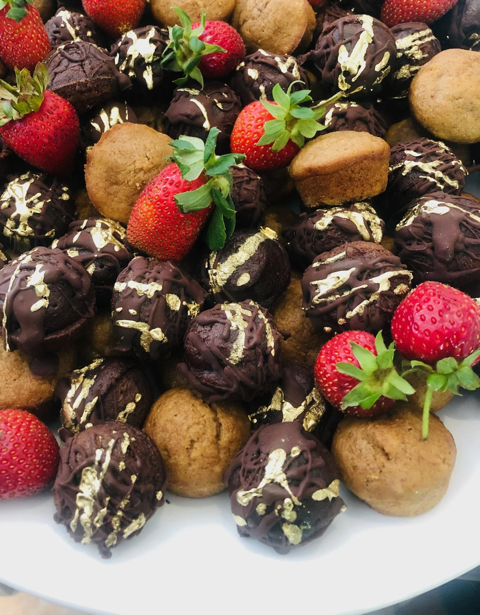 Assorted chocolate truffles topped with gold leaf, fresh strawberries, and small round cookies surrounding the treats.