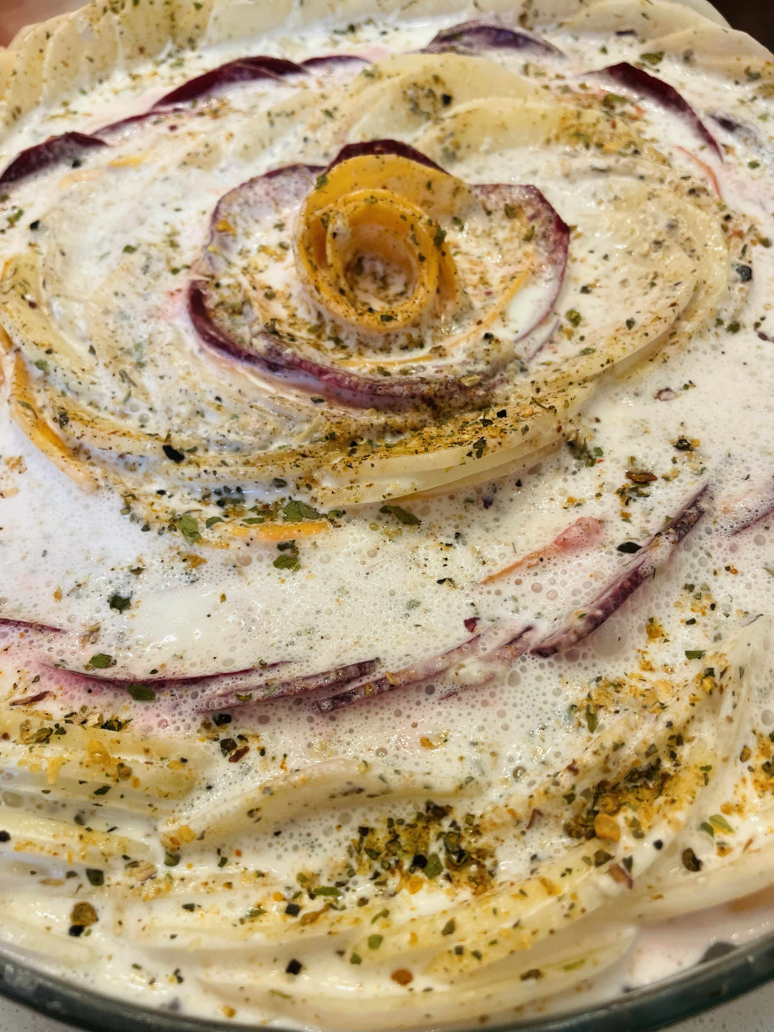 Close-up of a creamy vegetable and spice casserole with sliced onions and herbs on top.