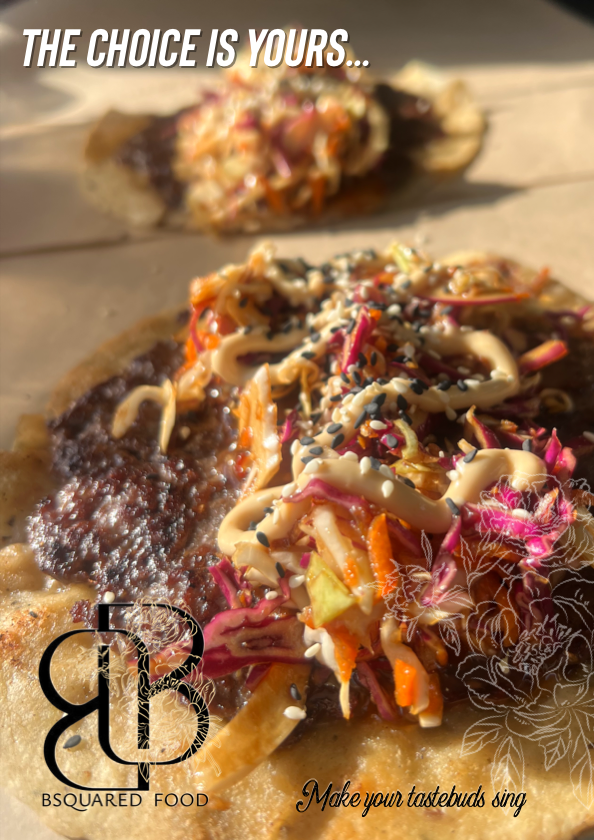 Close-up of two loaded tacos with various toppings like vegetables and sauce, on a wooden surface, with sunlight.