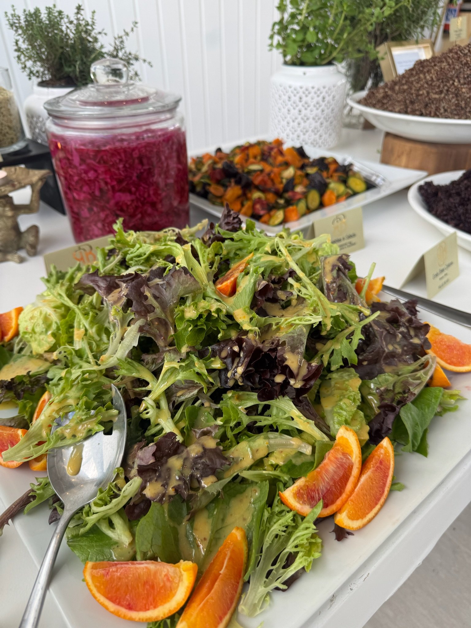 Fresh mixed green salad with orange slices on a white platter.