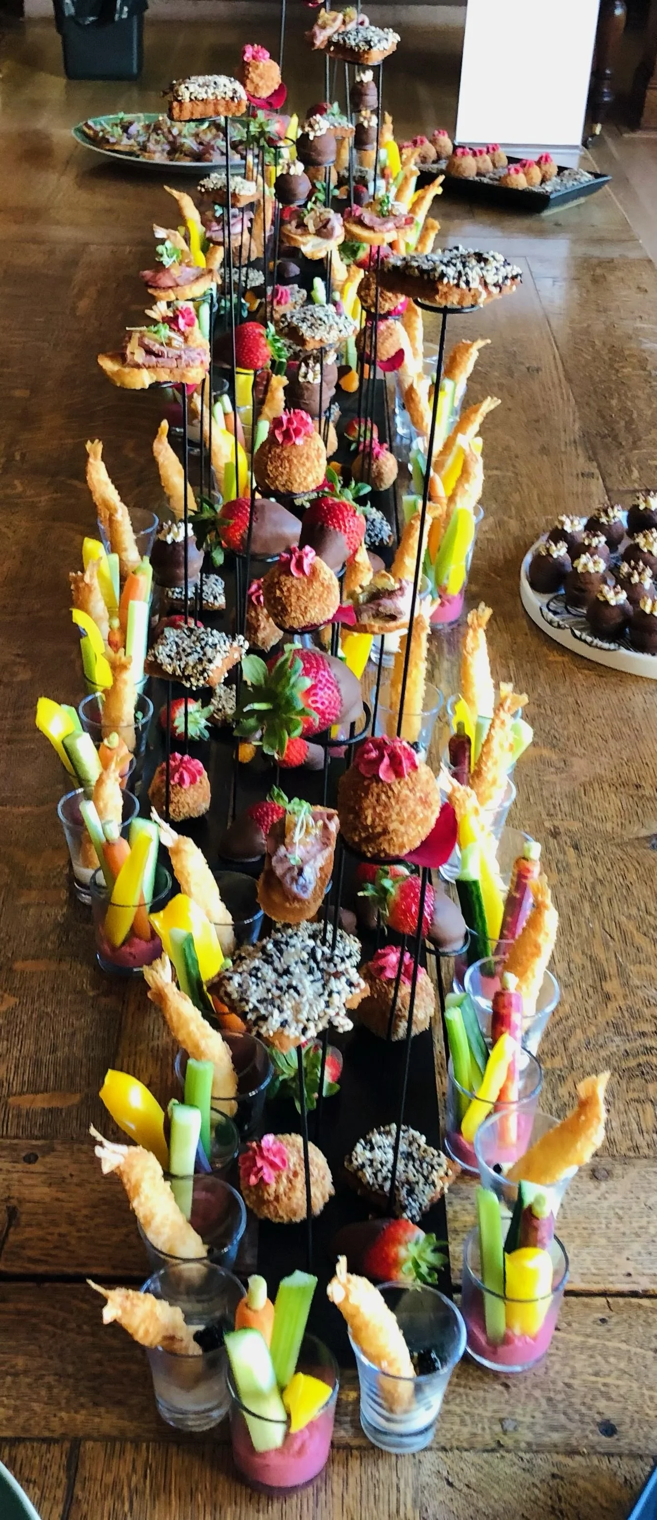 Colorful assortment of desserts including strawberries, cake pops, and finger foods on a tiered display at a party or event.