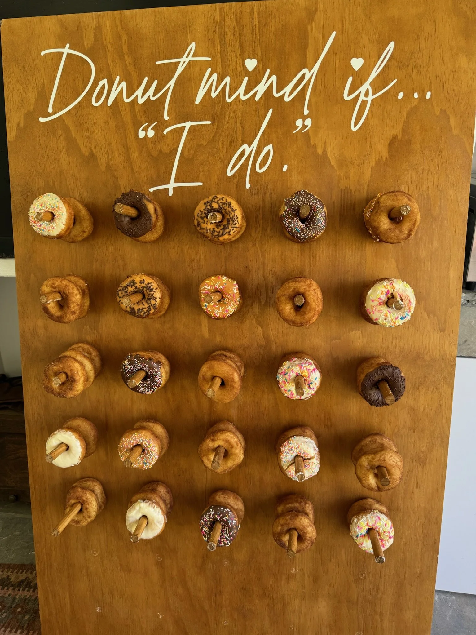 Display of various donuts on wooden board with a sign reading 'Donut mind if... I do.'