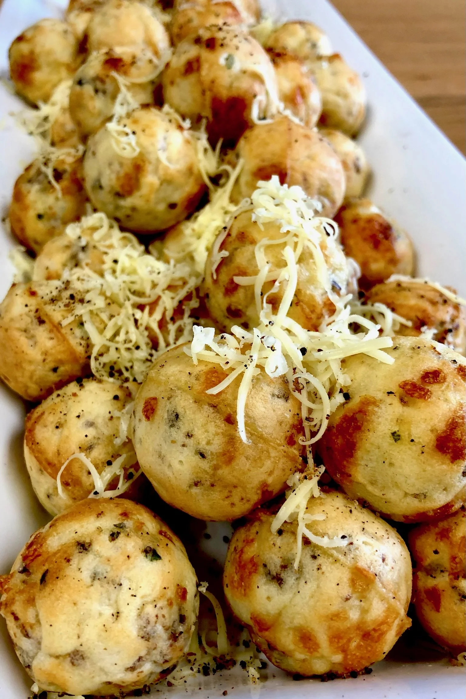 A plate of cooked meatballs topped with shredded cheese, garnished with black pepper.