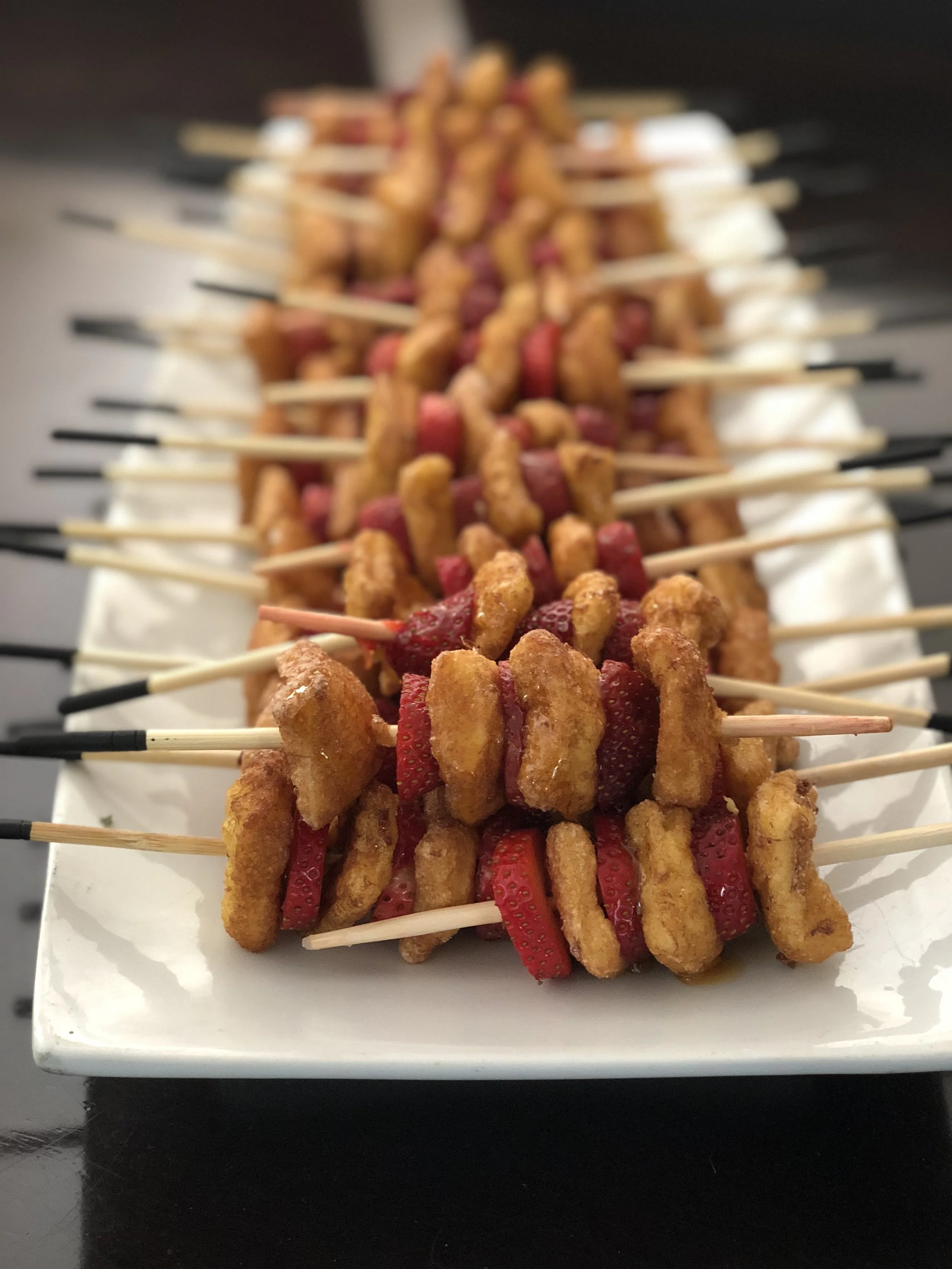 Skewers of French toast and strawberries on a rectangular white plate.