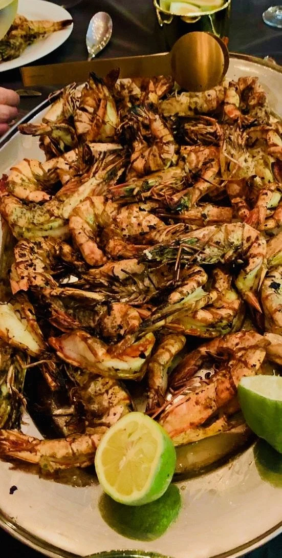 A large platter of grilled prawns, garnished with lemon and lime wedges.