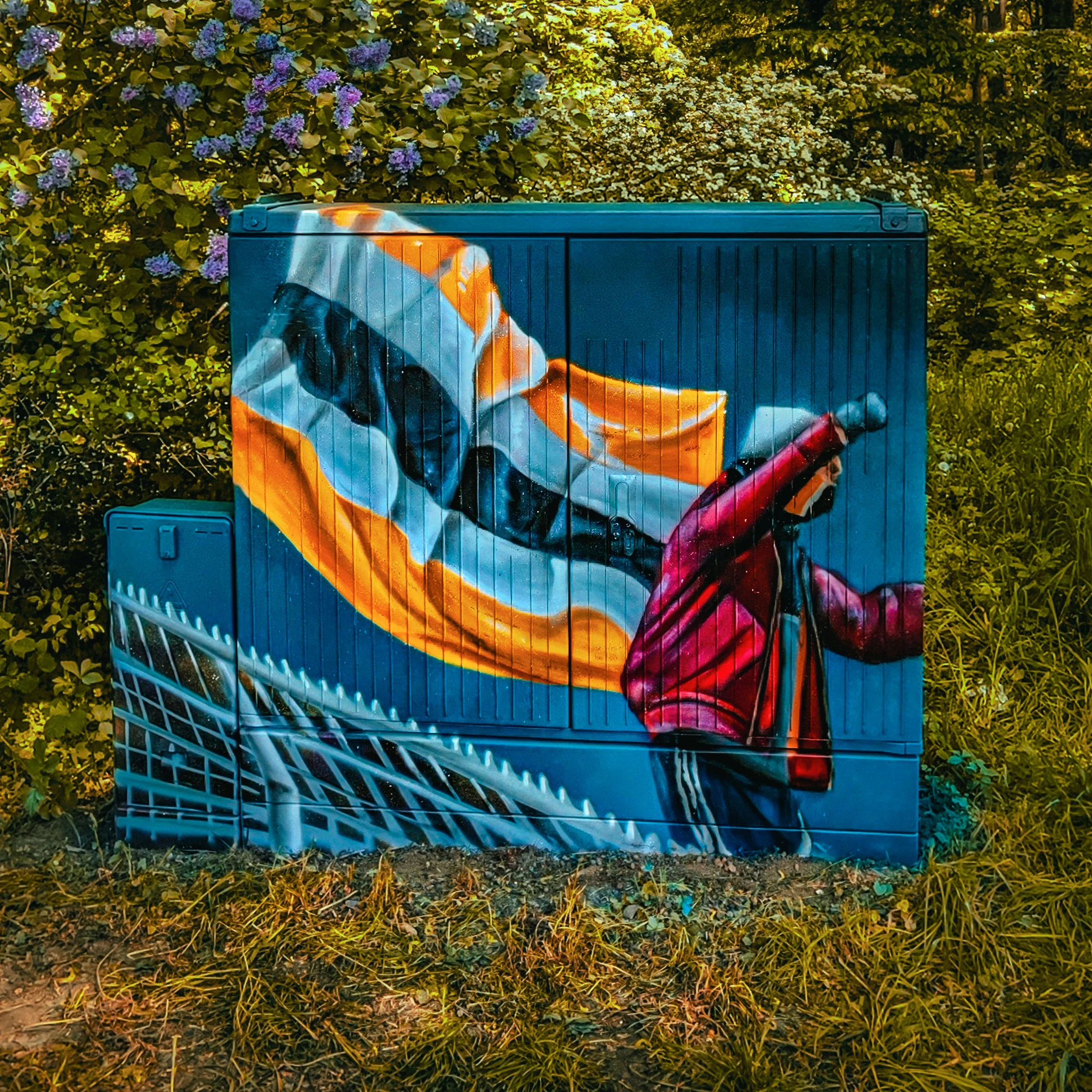 Straßenkunst mit einem Skateboardfahrer und einem Kind, das auf einem Skateboard im Park fährt, gemalt auf einer Verteilerdose im Freien.