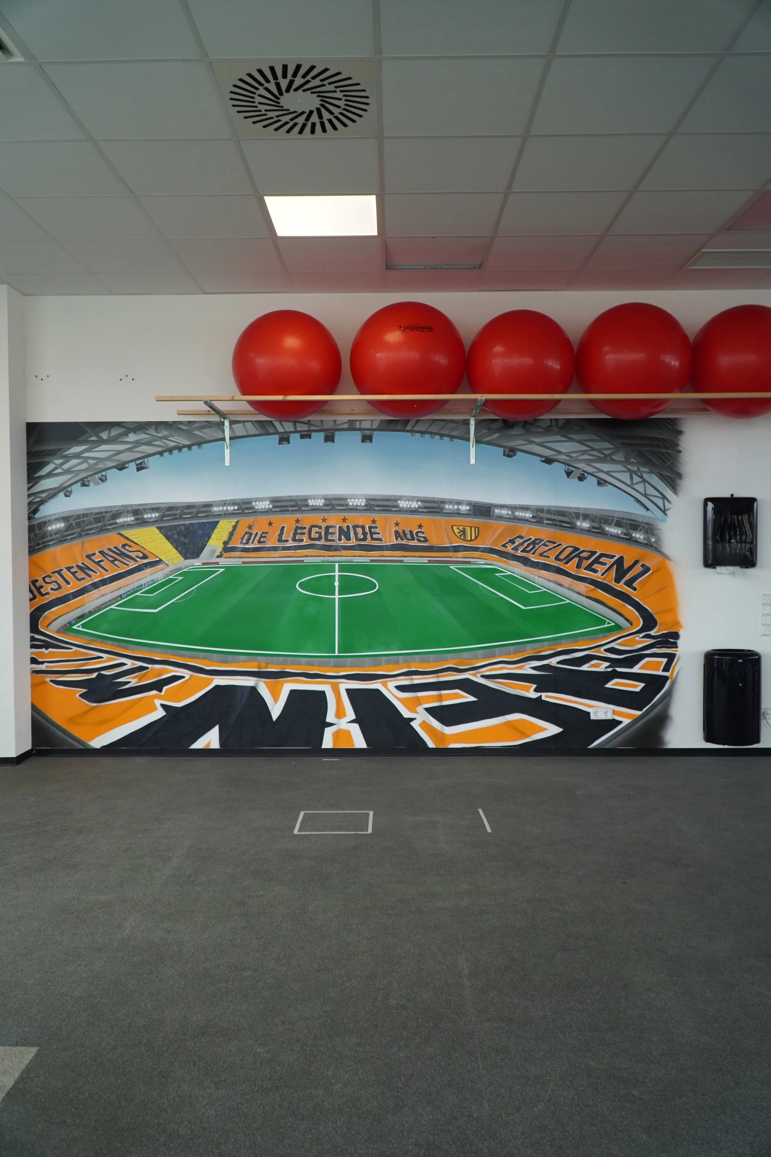 Wanddekoration mit einem Fußballstadion-Motiv und roten Gymnastikbällen an der Decke.