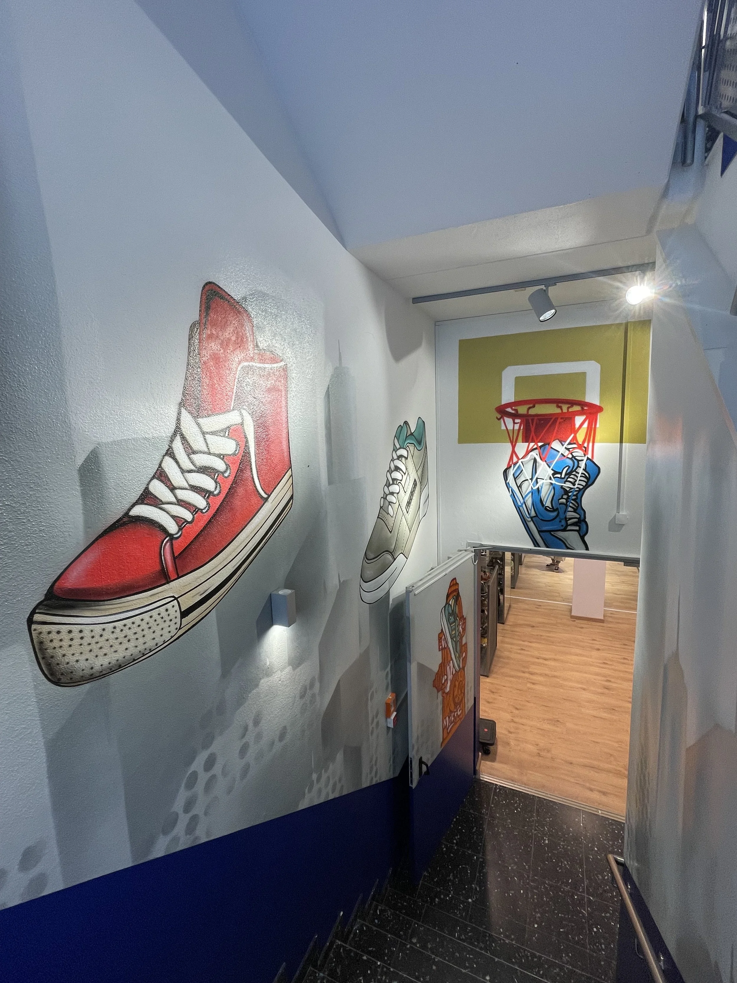 Innenaufnahme eines Treppenhauses mit Wandmalereien von Turnschuhen und einem Basketballkorb an der Wand.