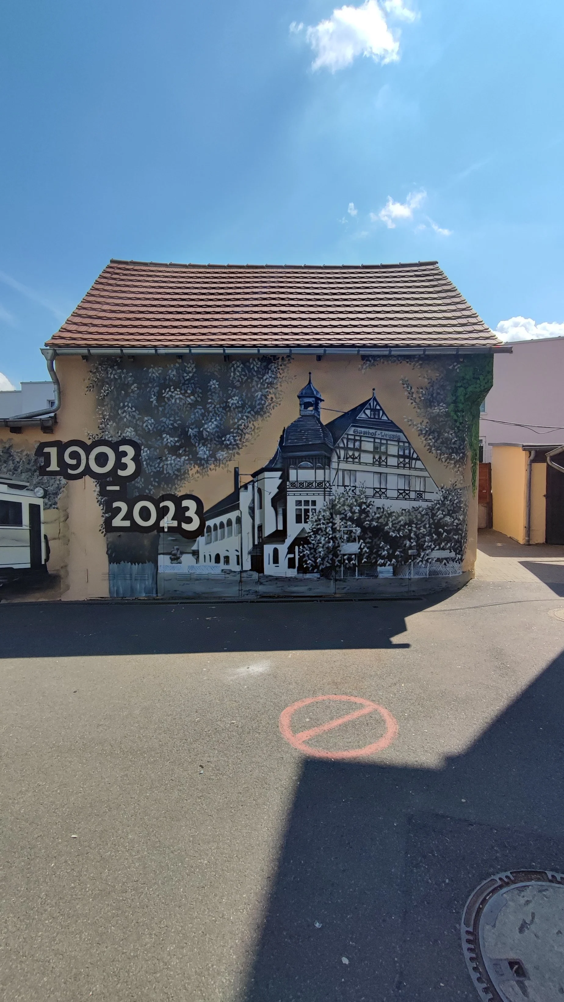 Wandgemälde an einer Hauswand zum Gedenken an 120 Jahre, mit Jahreszahlen 1903 und 2023, zeigt ein stilisiertes Haus mit Tradition.