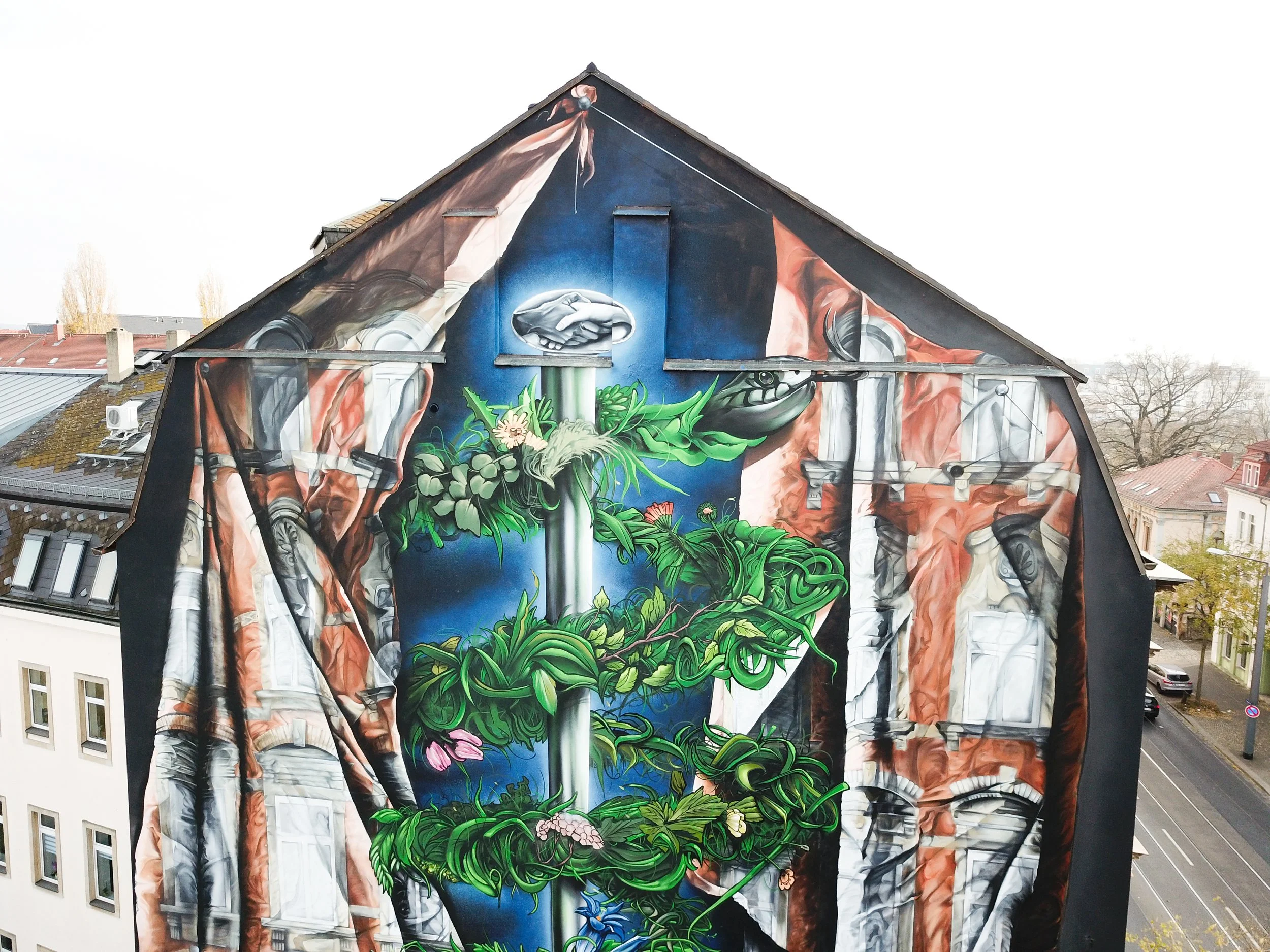 Wandbild auf einem Haus, das eine Mischung aus Natur und urbaner Kunst zeigt, mit grünen Pflanzen, einem Wasserfall und gefärbten Texturen.