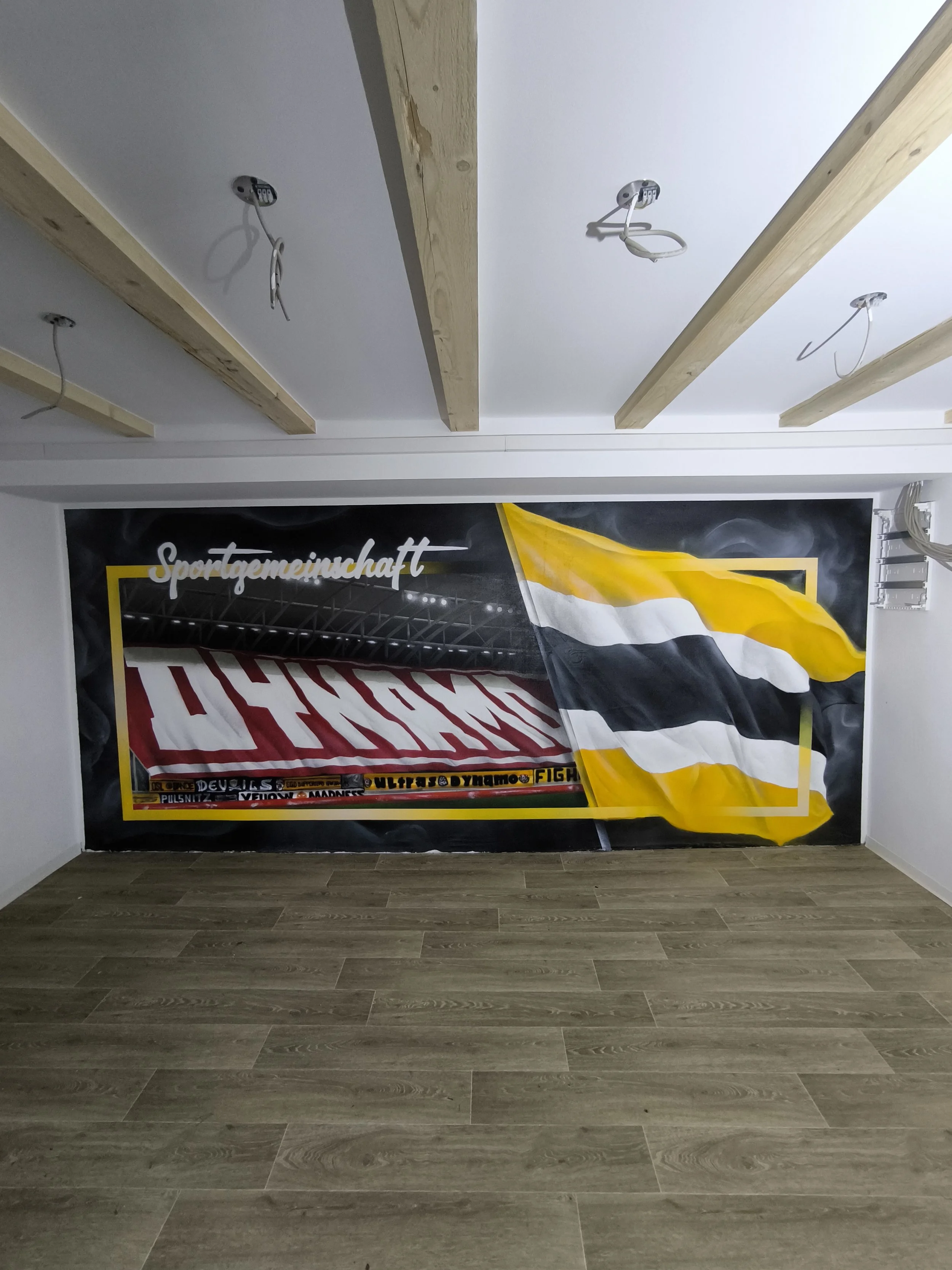 Ein Wandbild mit einem gestreiften Fanschal und einer Flagge in den Farben Gelb, Schwarz und Weiß, mit der Aufschrift 'Spartegemeinschaft'.