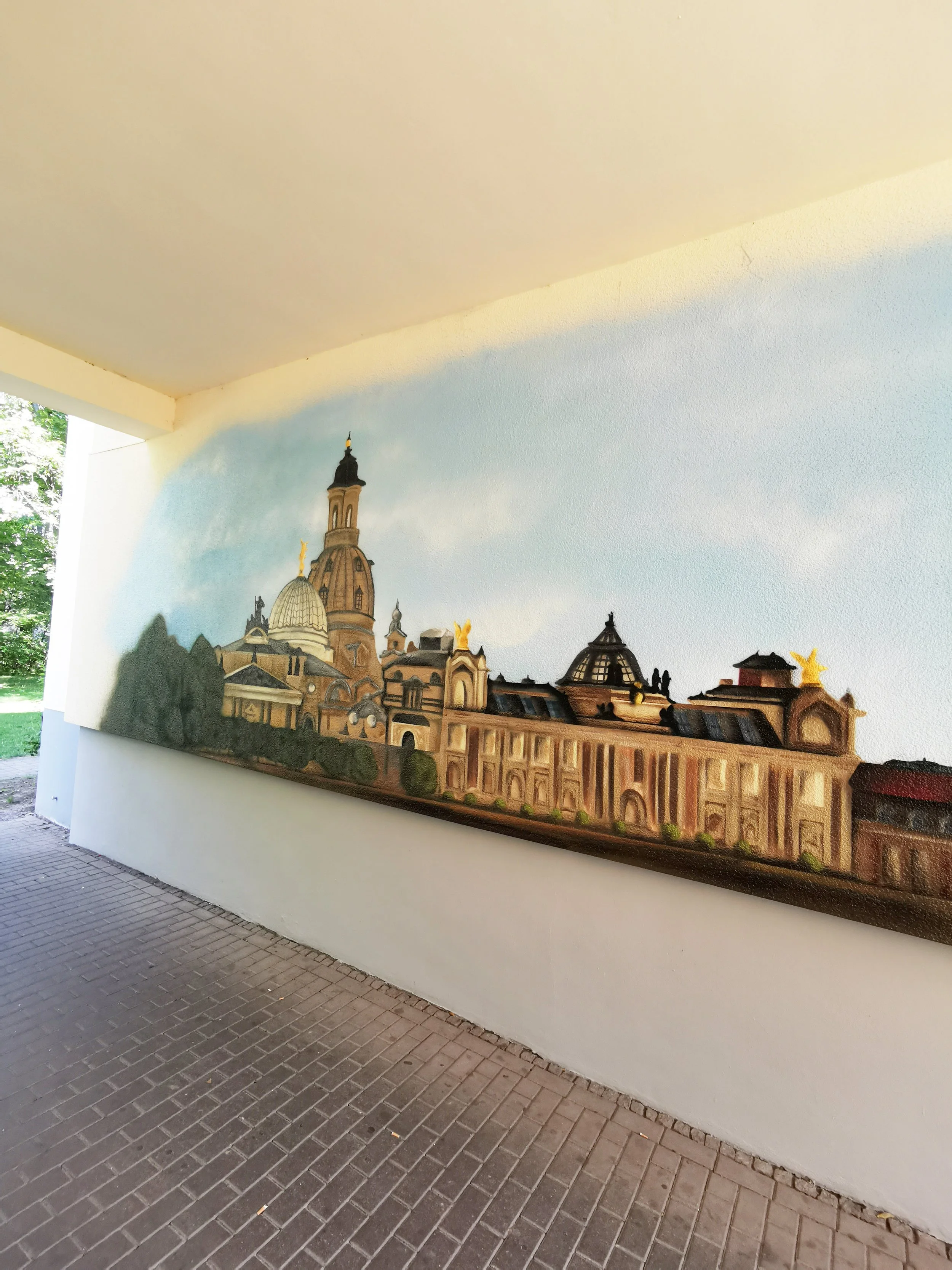 Straßenwandmalerei, die eine Panoramaansicht eines alten Stadtteils mit Kirchen und Gebäuden zeigt.