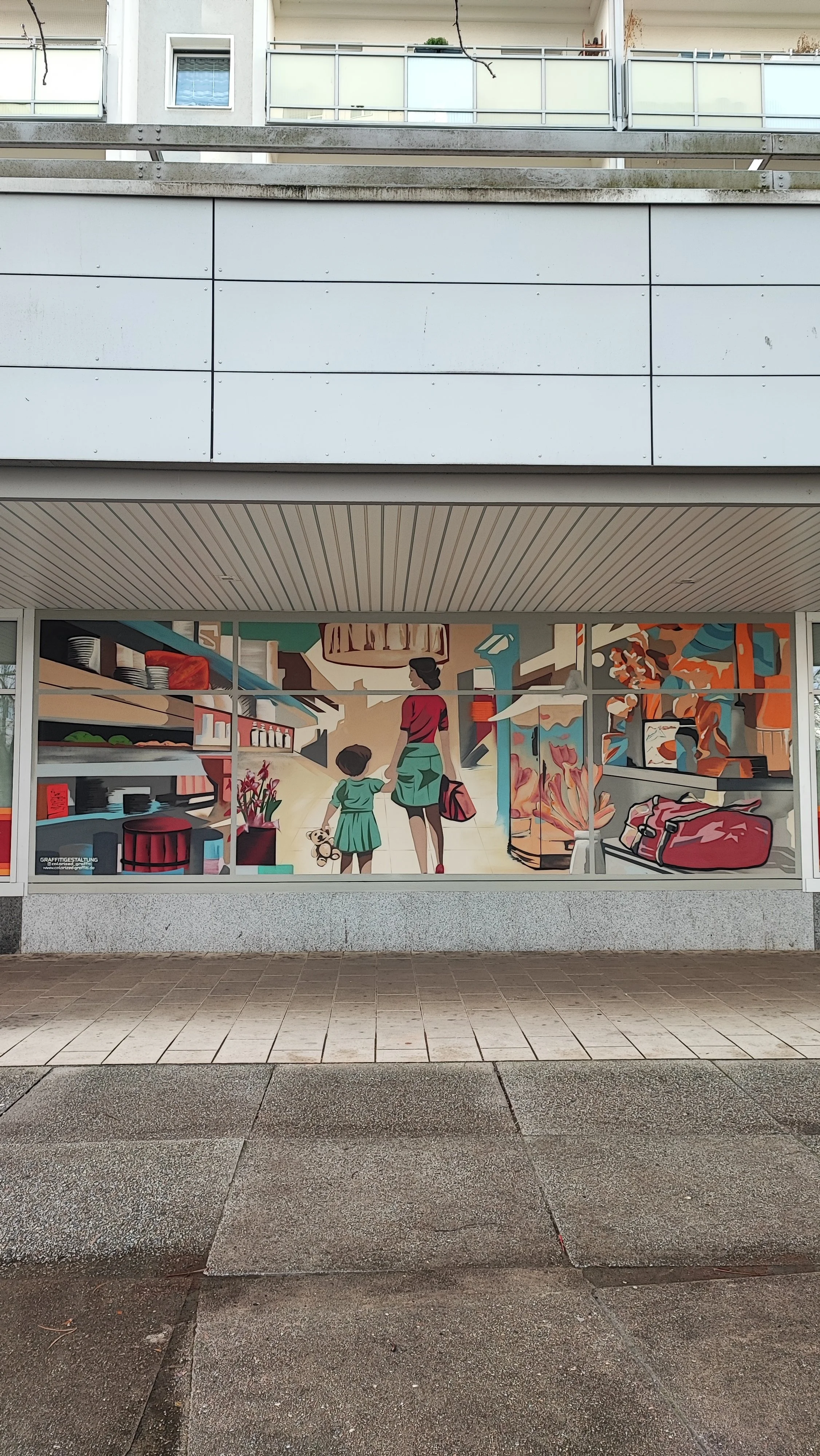 Fassade eines Geschäfts mit einer Wandmalerei, die eine Frau und ein Kind in einem Supermarkt zeigt.