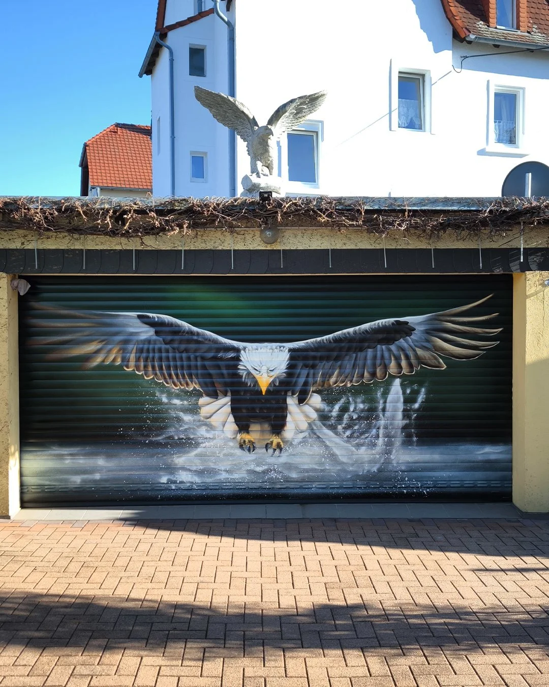 Lackiertes Garagentor mit realistischem Wandbild eines angreifenden Adlers, der in den Flug geht, mit Wasser spritzend im Hintergrund.