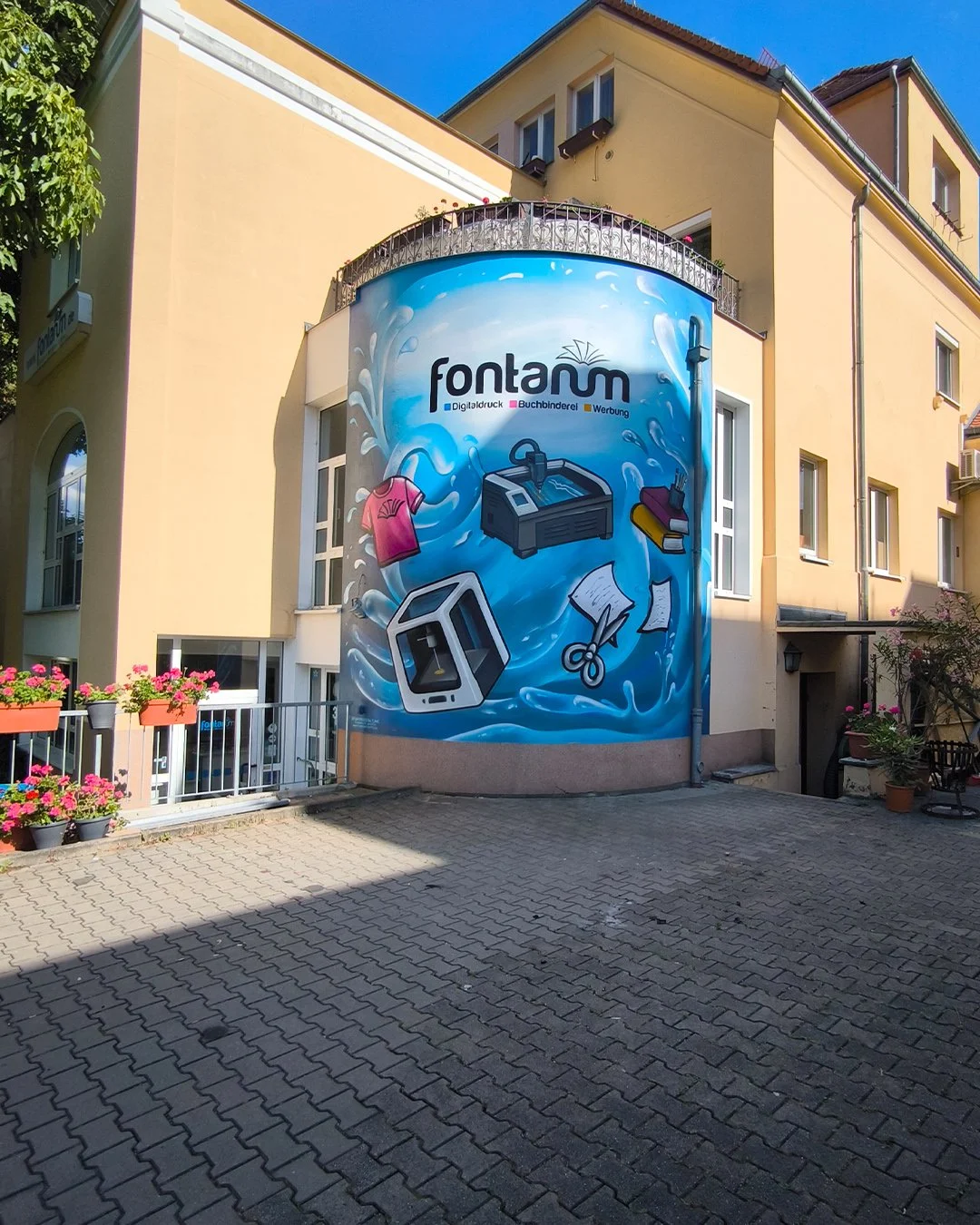 Mehrfarbige Wandmalerei an einem runden Gebäude mit dem Text "fontam" und Symbolen für Druck, Buchbinderei und Werbung Dresden