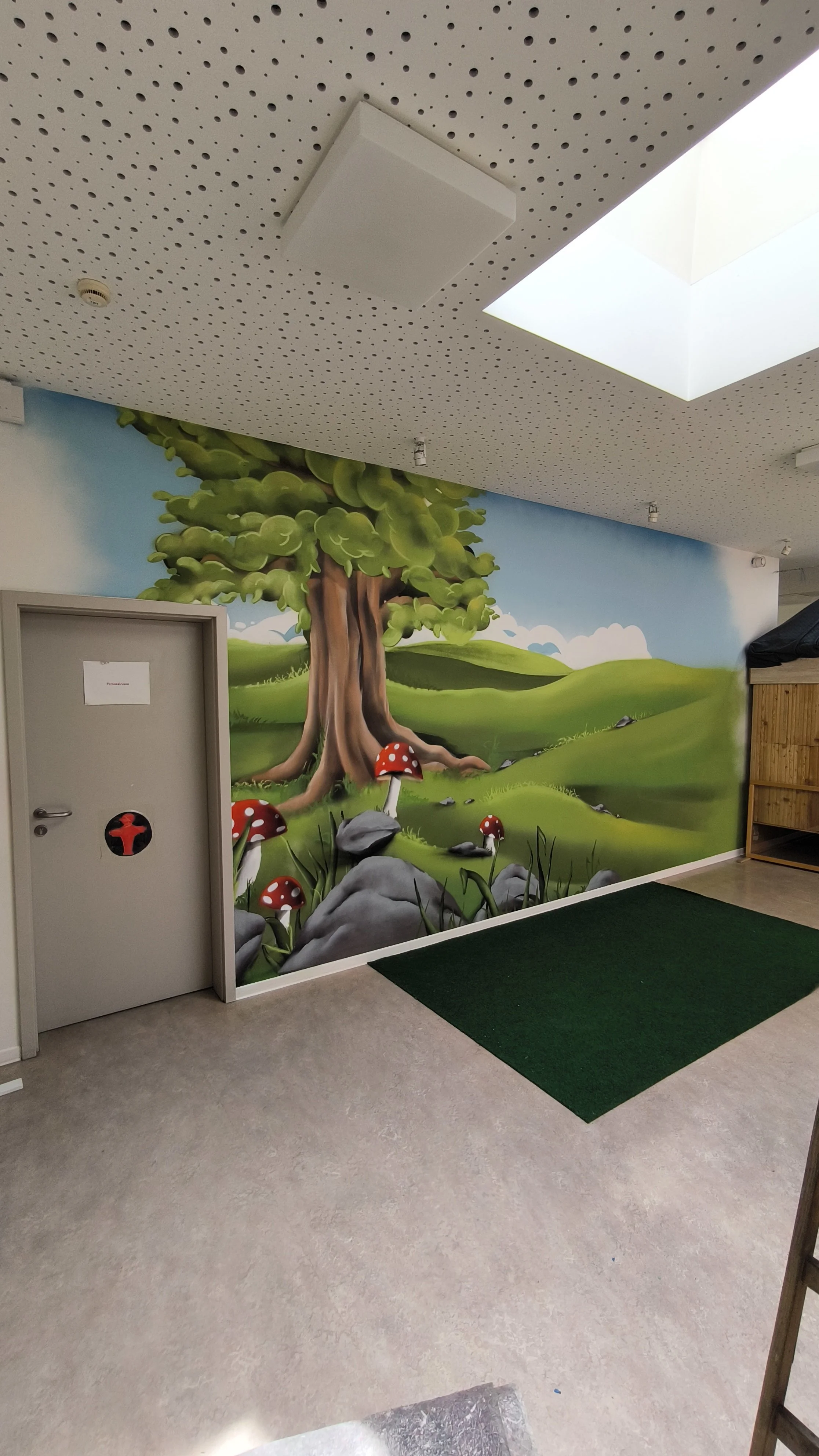 Wandbemalung eines Waldes mit einem großen Baum und Pilzen im Vordergrund in einem Raum.